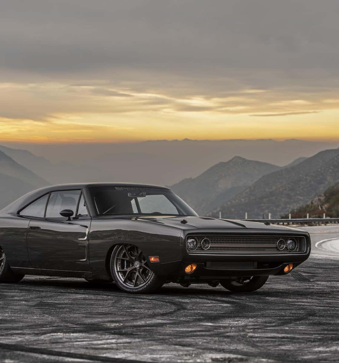 Dodge 桌布 壁紙 — 一架時尚黑色肌肉車在日落時分的山路上飄移，背景是橙色的天空和霧氣繚繞的山峰。