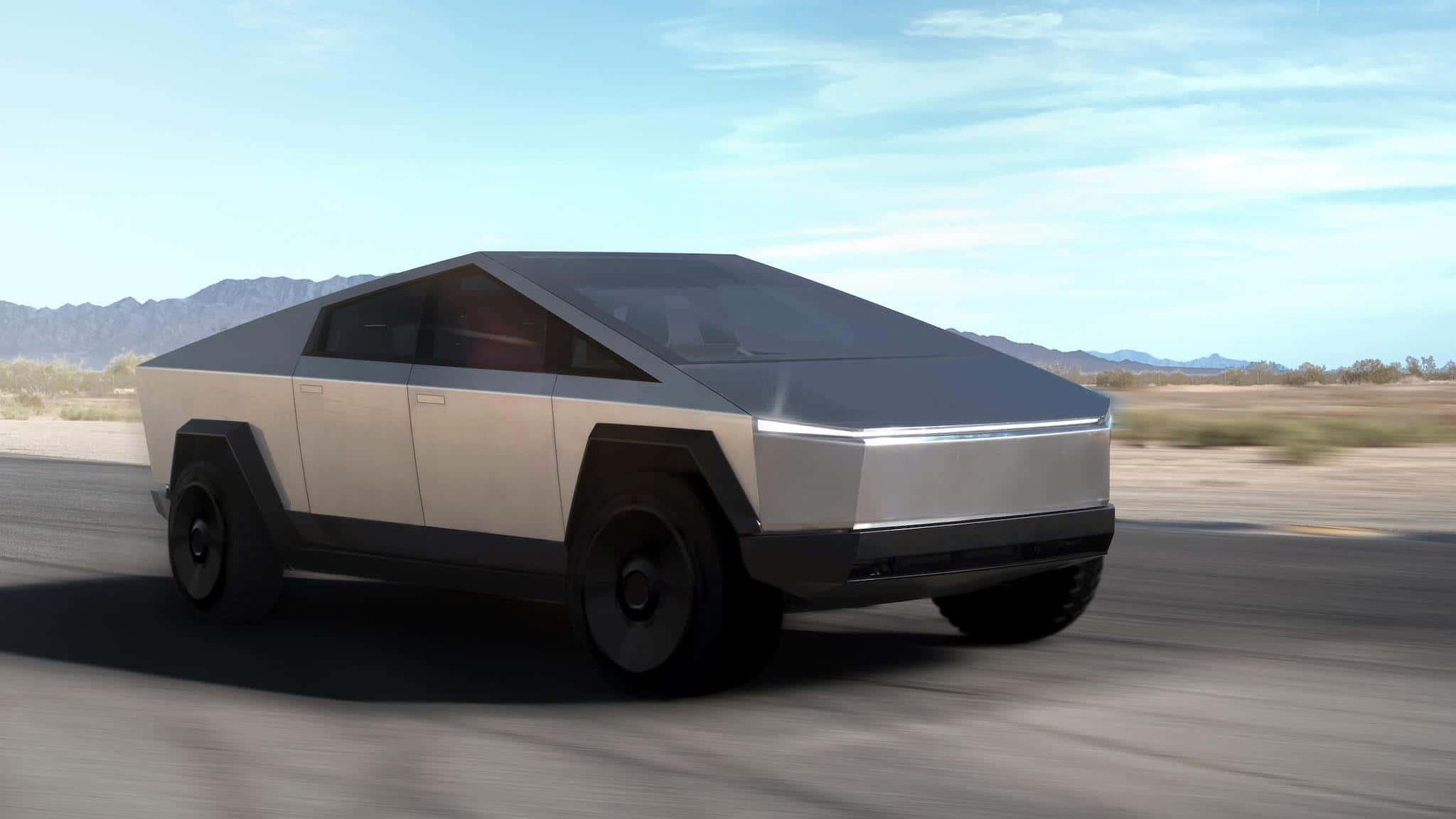 Cybertruck 桌布 壁紙 — 一架未來感十足的銀色 Tesla Cybertruck 在沙漠公路上疾馳，背景是山脈，天空清澈湛藍。