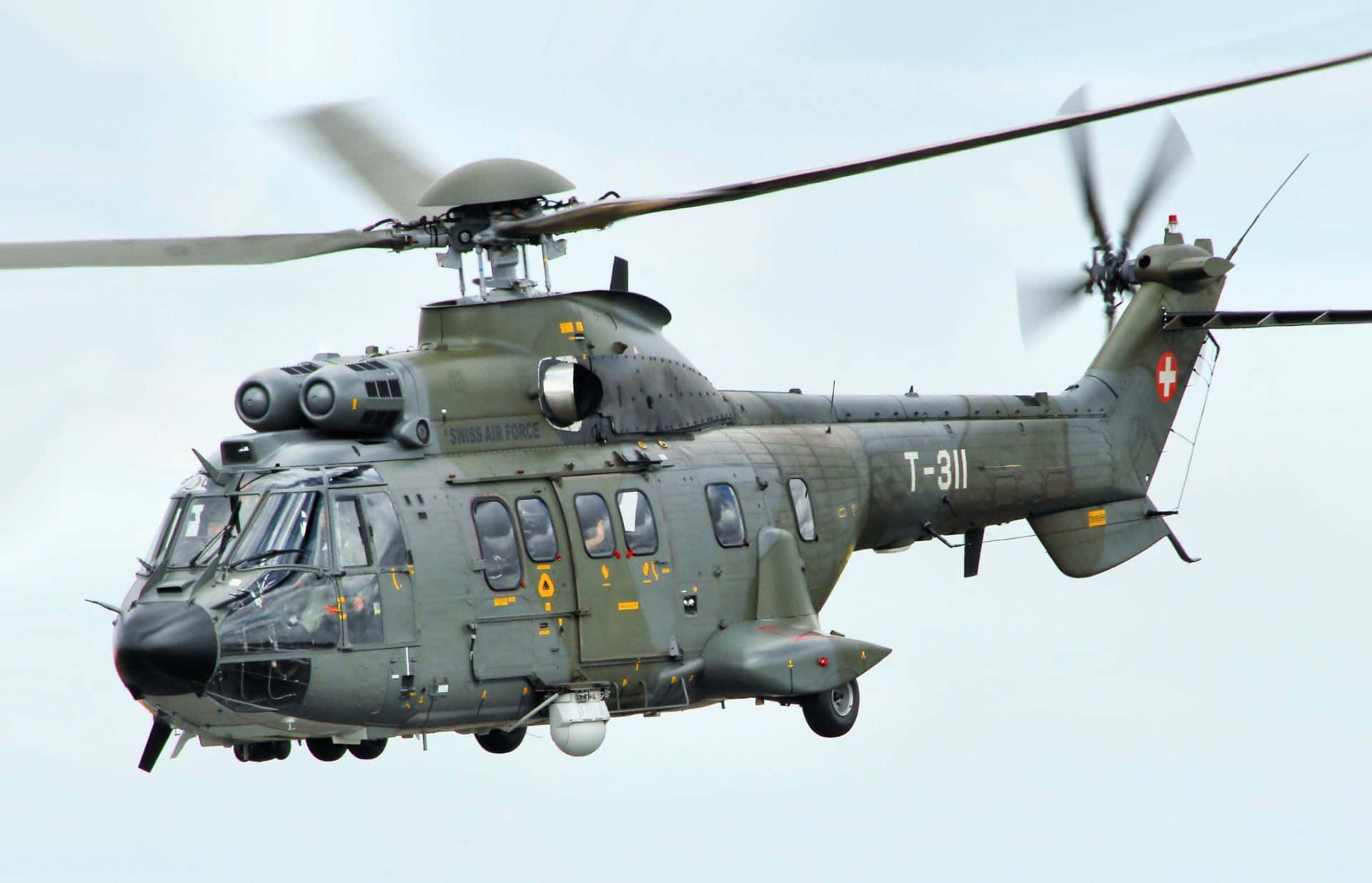Helicopter 桌布 壁紙 — 一架橄欖綠色的瑞士空軍軍用直升機在蒼白的天空中飛行，旋翼旋轉。