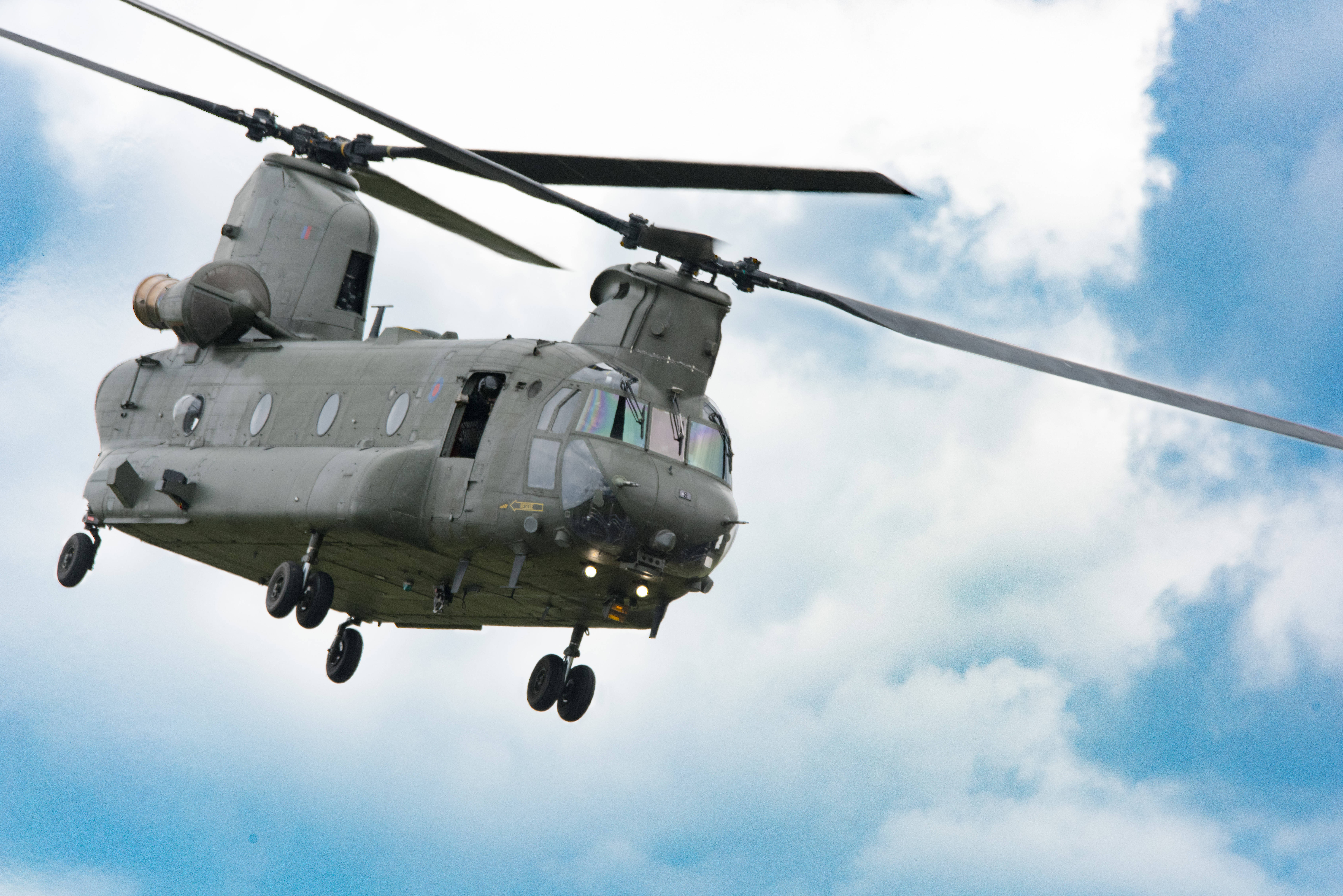 helicopter 4K 桌布 壁紙 — 一架橄欖綠色的軍用直升機在晴朗的藍天和 fluffy 白雲中低飛。