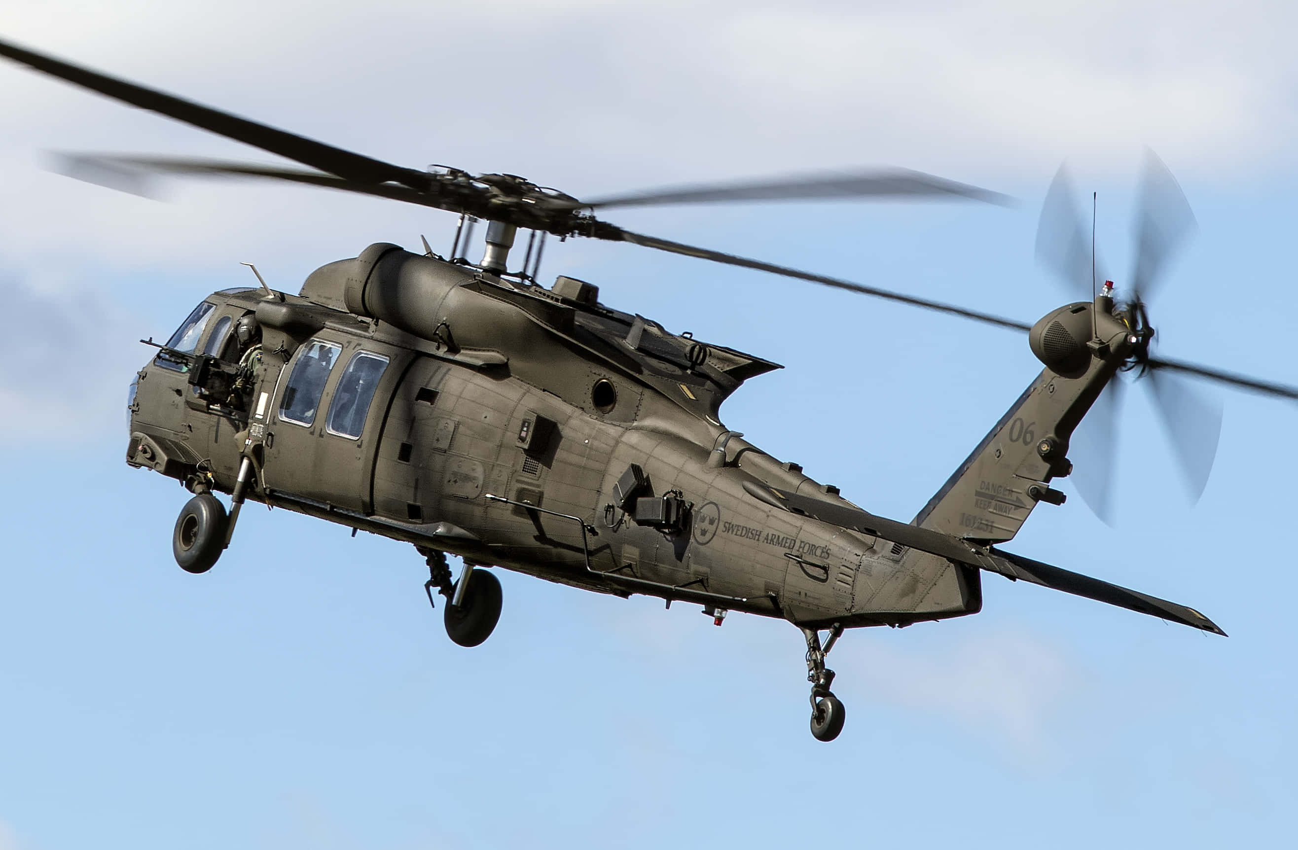Helicopters 桌布 壁紙 — 一架橄欖綠色的軍用直升機在晴朗的藍天下飛行，旋翼轉動，起落架放下。