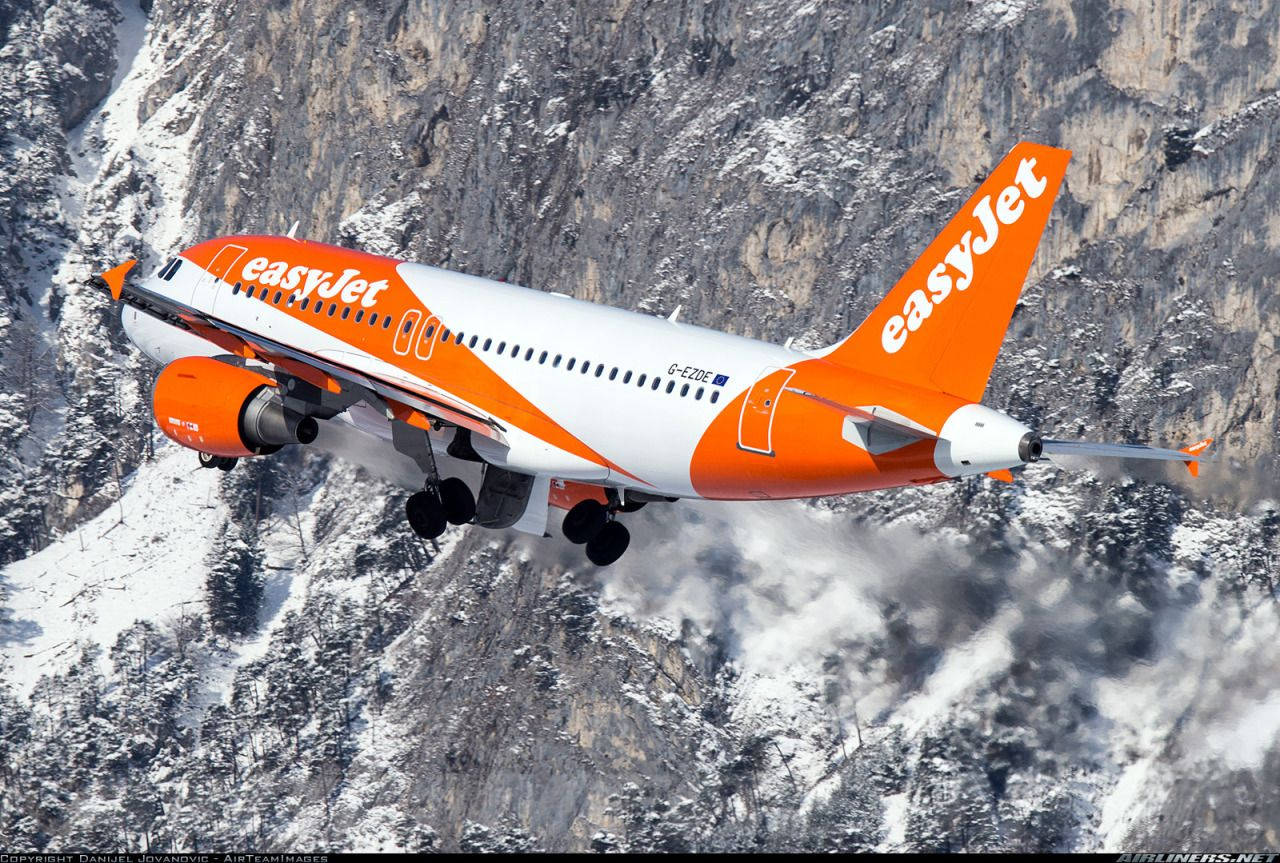 飛機 桌布 壁紙 — 一架橙色和白色的易捷航空飛機低飛越過積雪的山崖，起落架清晰可見。