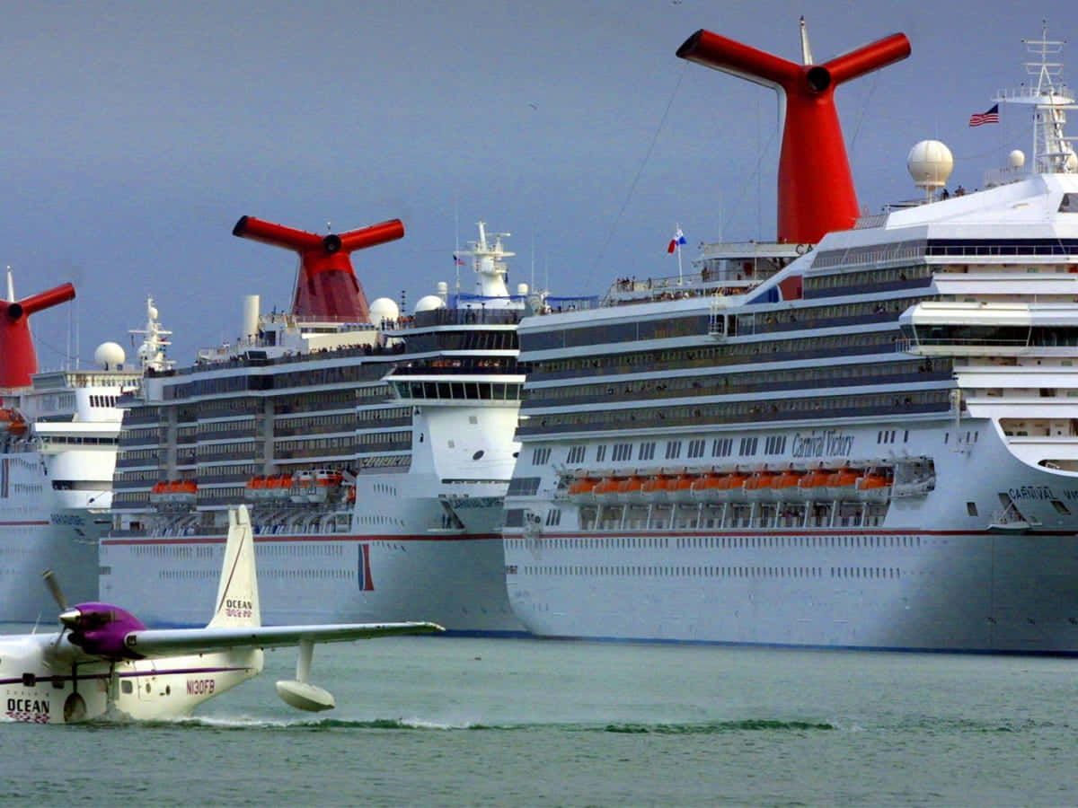 Carnival Dream 桌布 壁紙 — 一架水上飛機滑過停泊在平靜水域、帶有標誌性紅色煙囪的巨大嘉年華遊輪，天空晴朗。