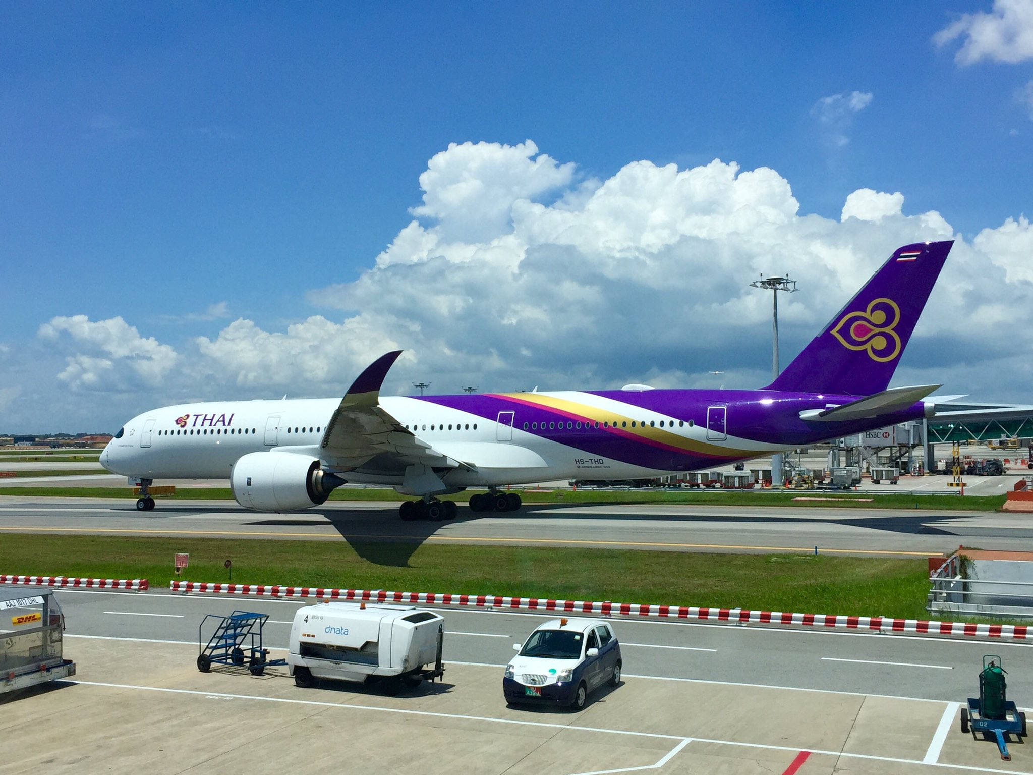 飛機 桌布 壁紙 — 一架泰國航空波音787夢幻客機在陽光明媚的機場停機坪上滑行，背景是明亮的藍天和蓬鬆的白雲。