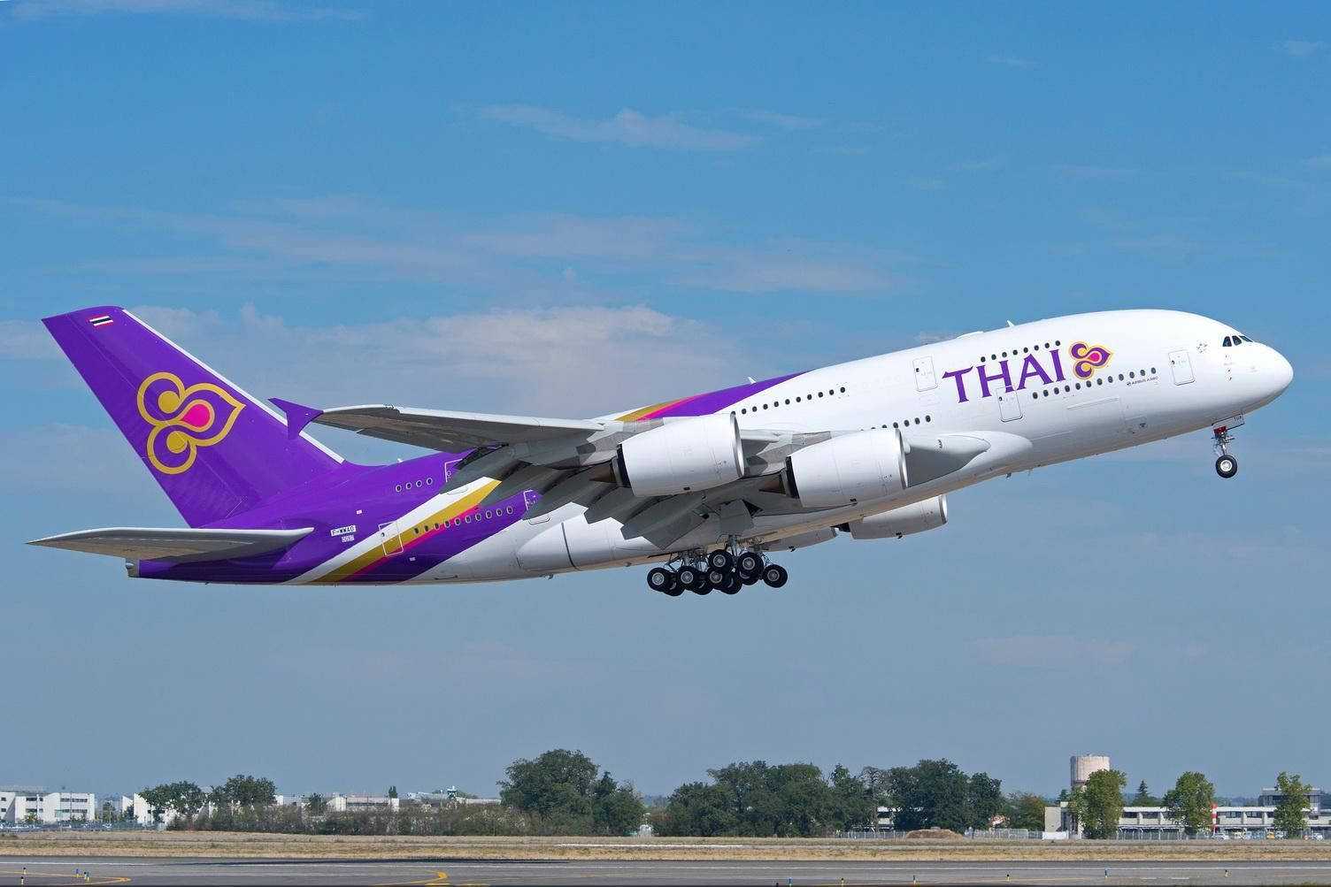  壁紙 — 一架泰國航空的空中巴士A380，採用紫色和白色塗裝，在晴朗的藍天下起飛，下方是跑道和樹木。