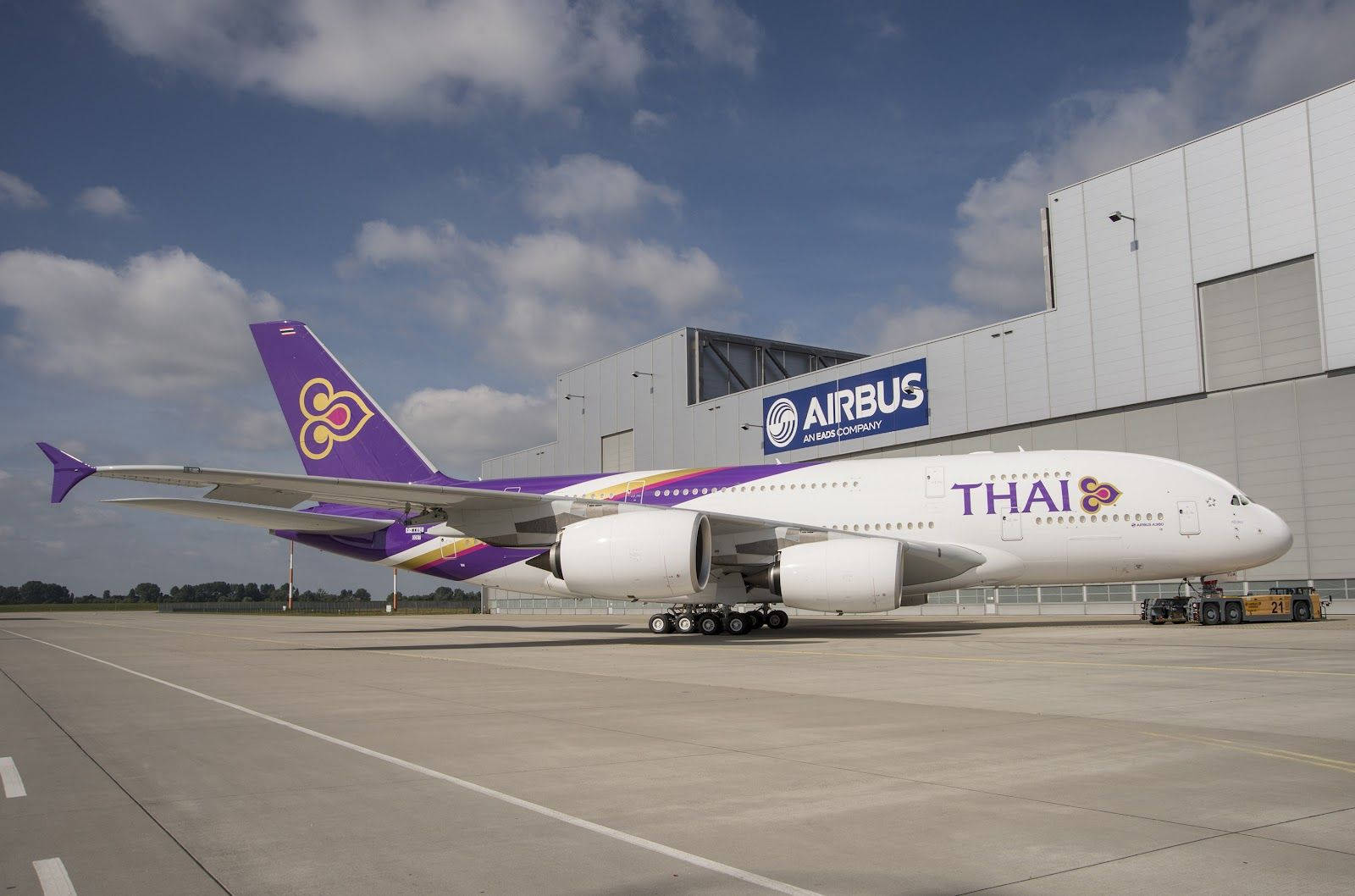 飛機 桌布 壁紙 — 一架泰國航空的空中巴士A380停泊在機場停機坪上，背景是部分多雲的藍天和一個機庫。