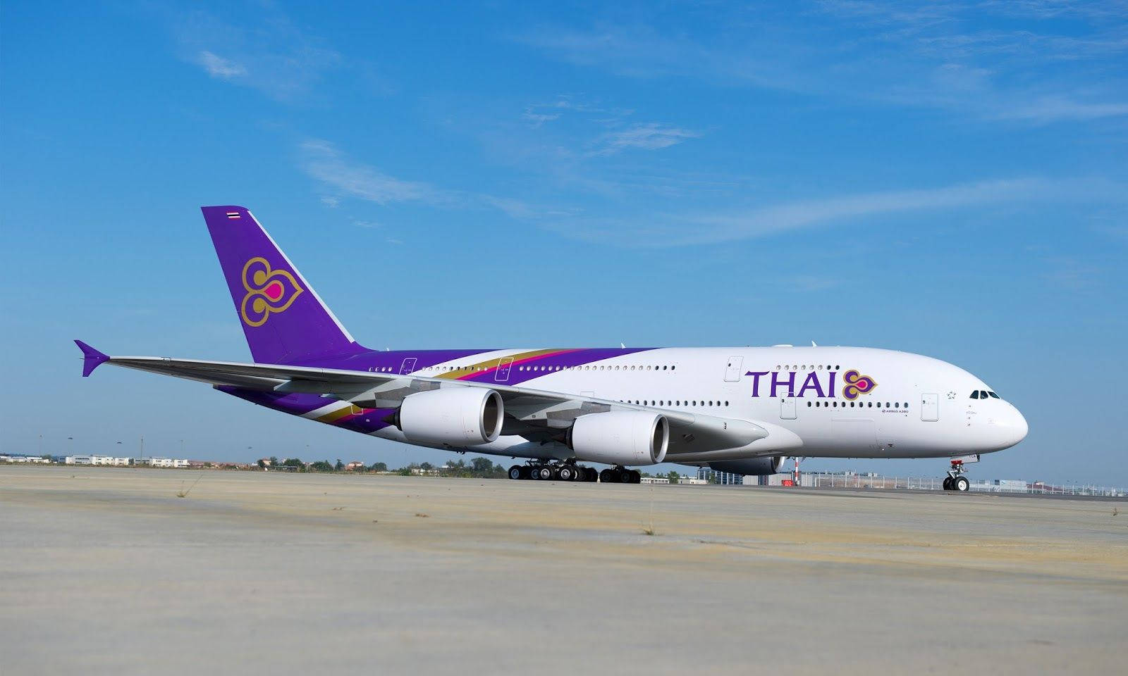 Airport 桌布 壁紙 — 一架泰國航空的空中巴士A380在陽光普照的停機坪上，背景是晴朗的藍天和薄雲。