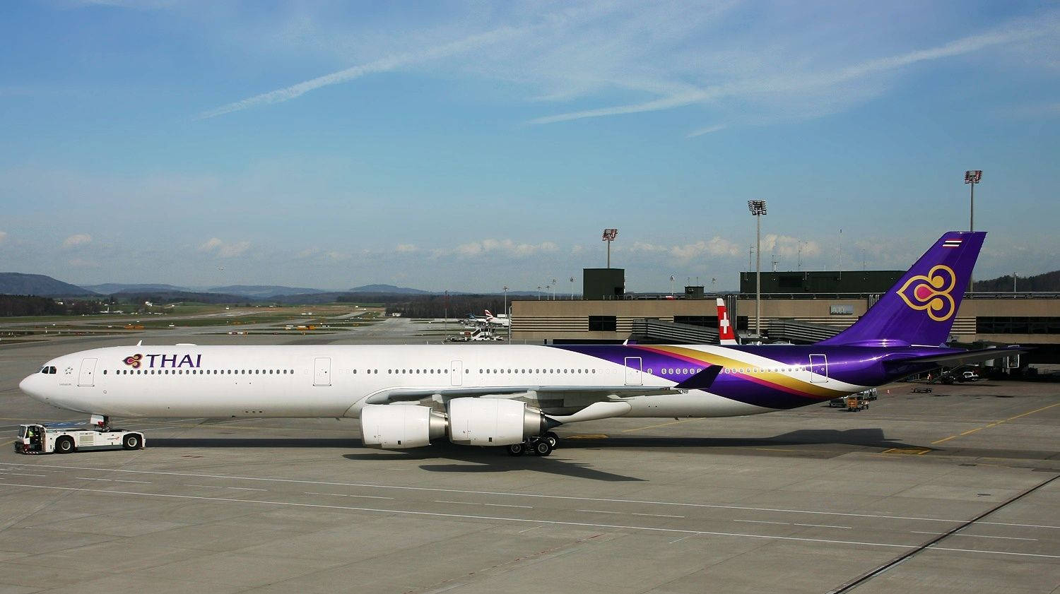 Airport 桌布 壁紙 — 一架泰國航空空中巴士A330停泊在機場停機坪上，天空清澈湛藍，遠處有山丘。