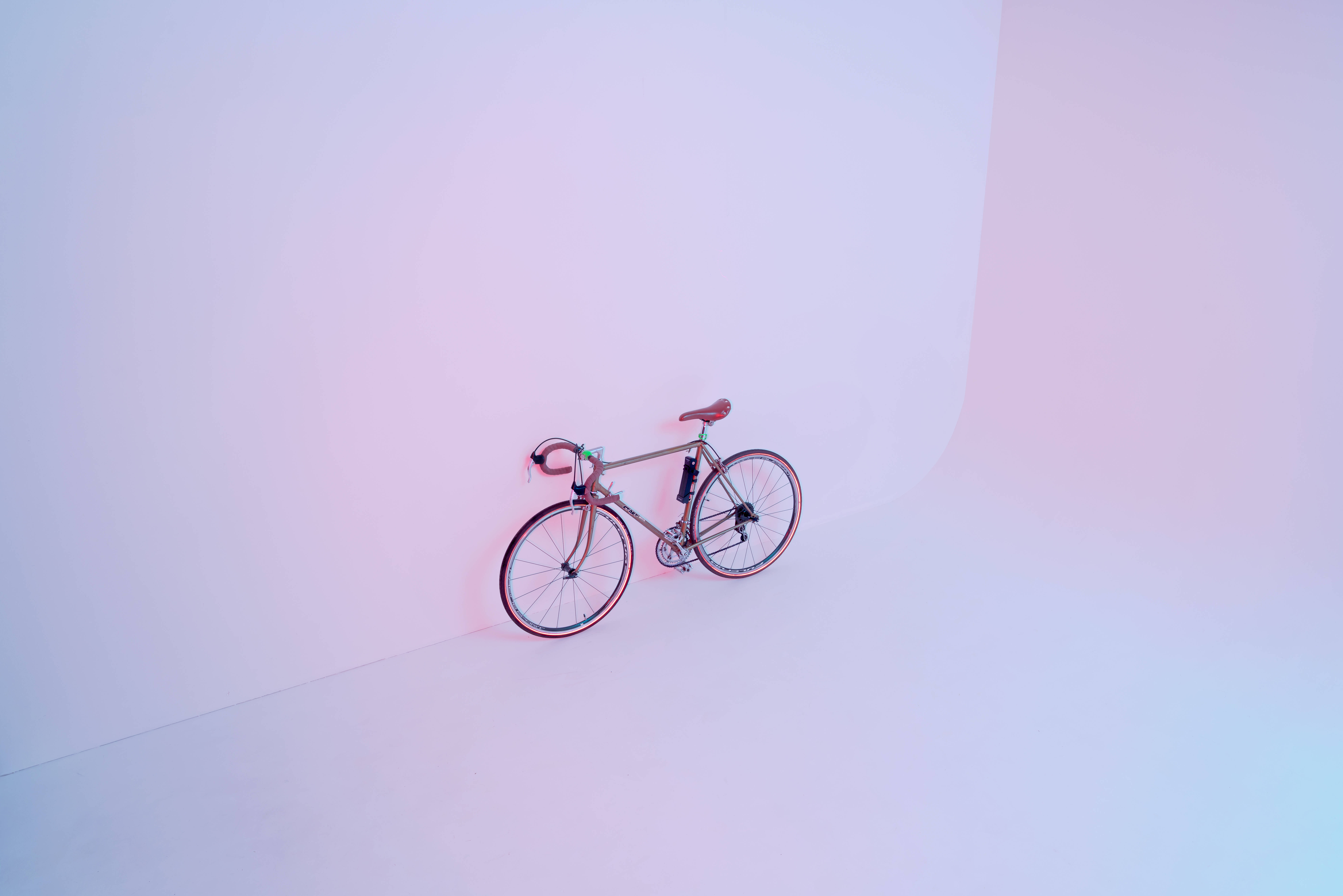 cute pastel colors 桌布 壁紙 — 一架流線型公路自行車停放在極簡工作室的角落，沐浴在柔和粉紅與藍色漸變燈光中。