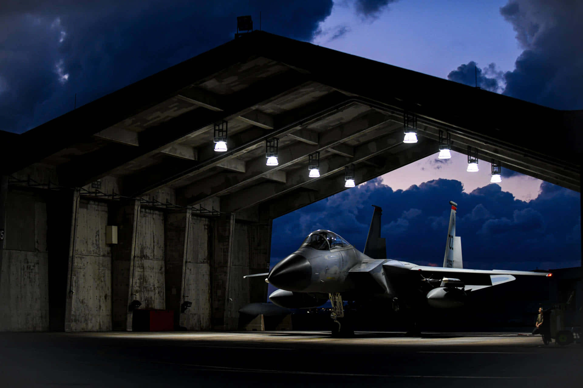 Air Force 桌布 壁紙 — 一架流線型戰鬥機停在昏暗的機庫內，暮色將天空染成深藍和紫色。