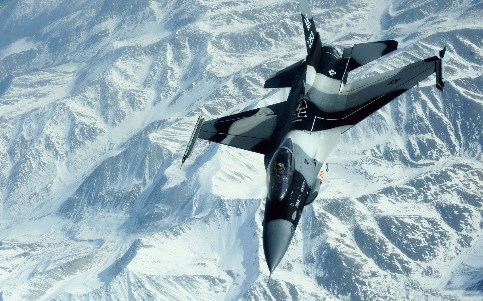 山脈 桌布 壁紙 — 一架流線型戰鬥機在晴朗天空下翱翔於廣闊的雪山山脈之上。