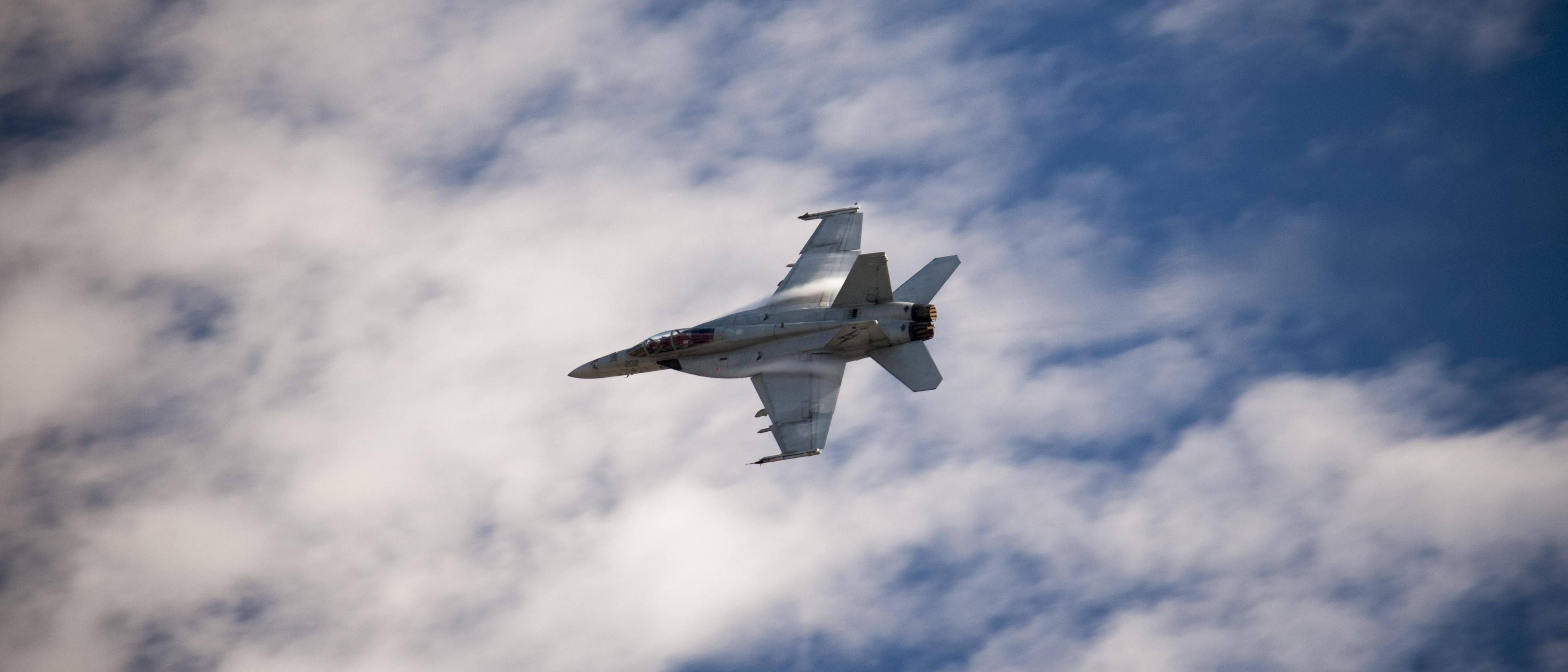  壁紙 — 一架流線型戰鬥機在藍天白雲的動態天空中翱翔。