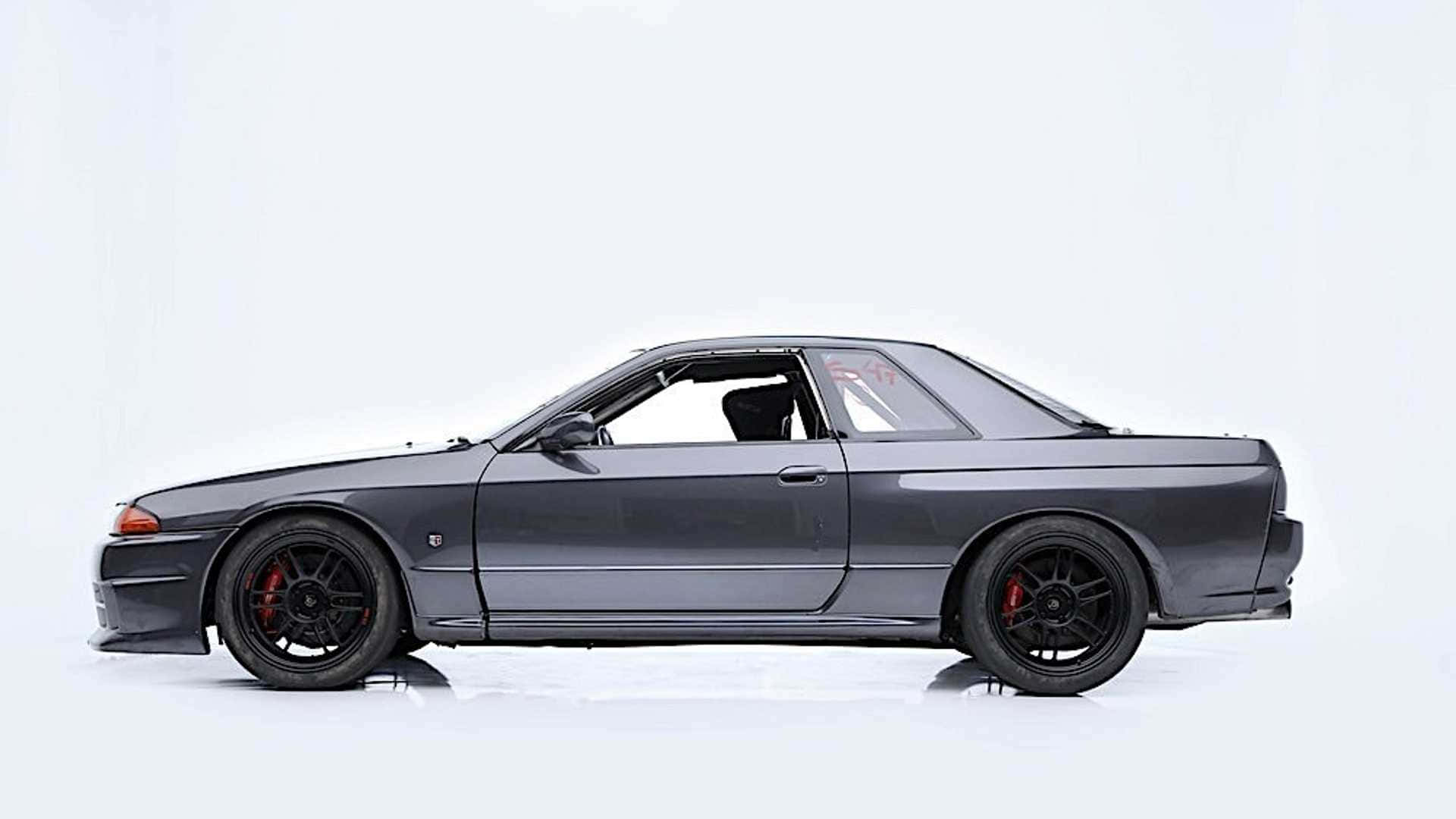 Paul Walker Skyline 桌布 壁紙 — 一架流線型深灰色日產Skyline GT-R跑車，配備黑色輪圈和紅色制動卡鉗，矗立在簡約的白色工作室中。