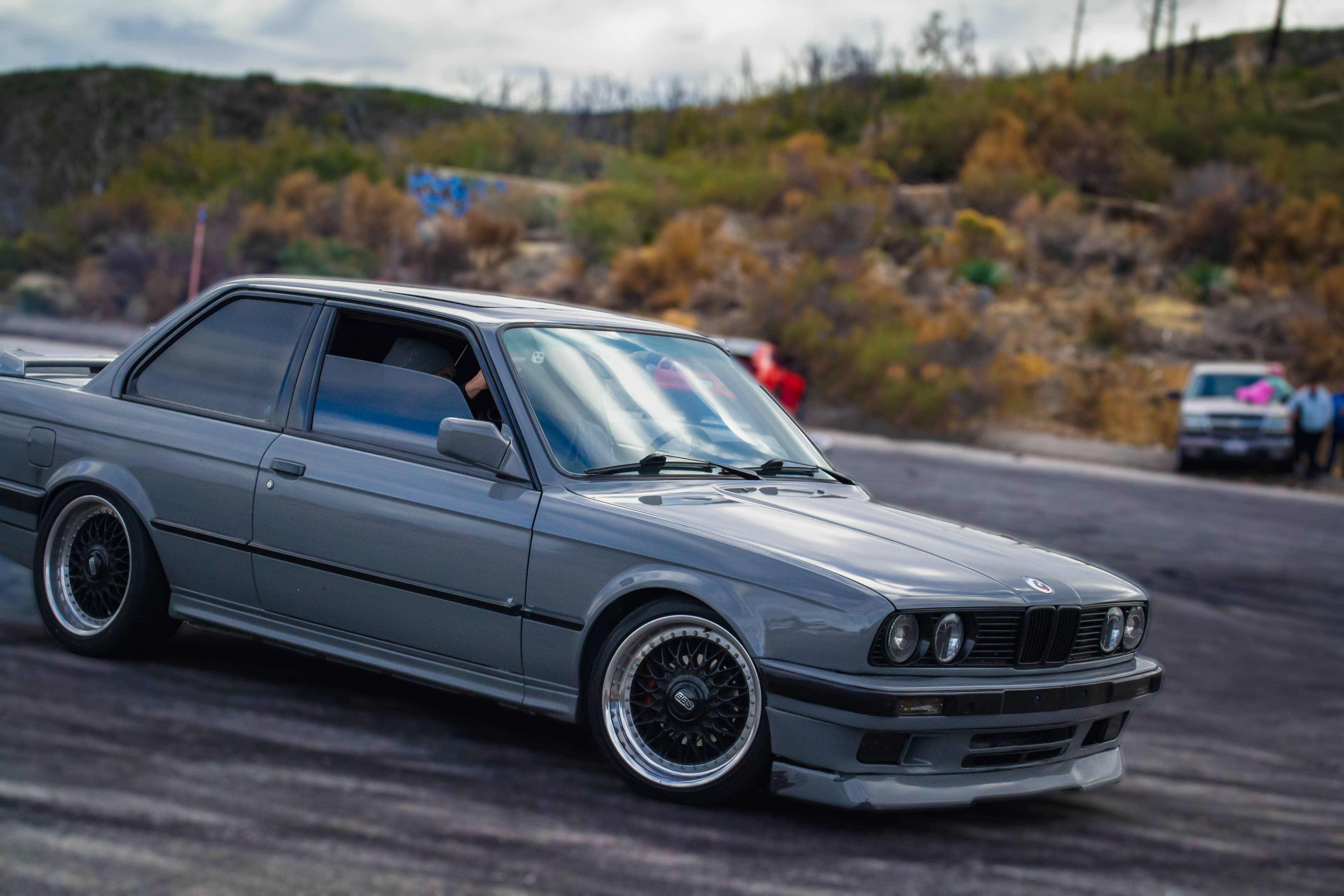 mustang HD 桌布 壁紙 — 一架流線型灰色BMW E30在鋪設的賽道上飄移，背景是秋色山丘。