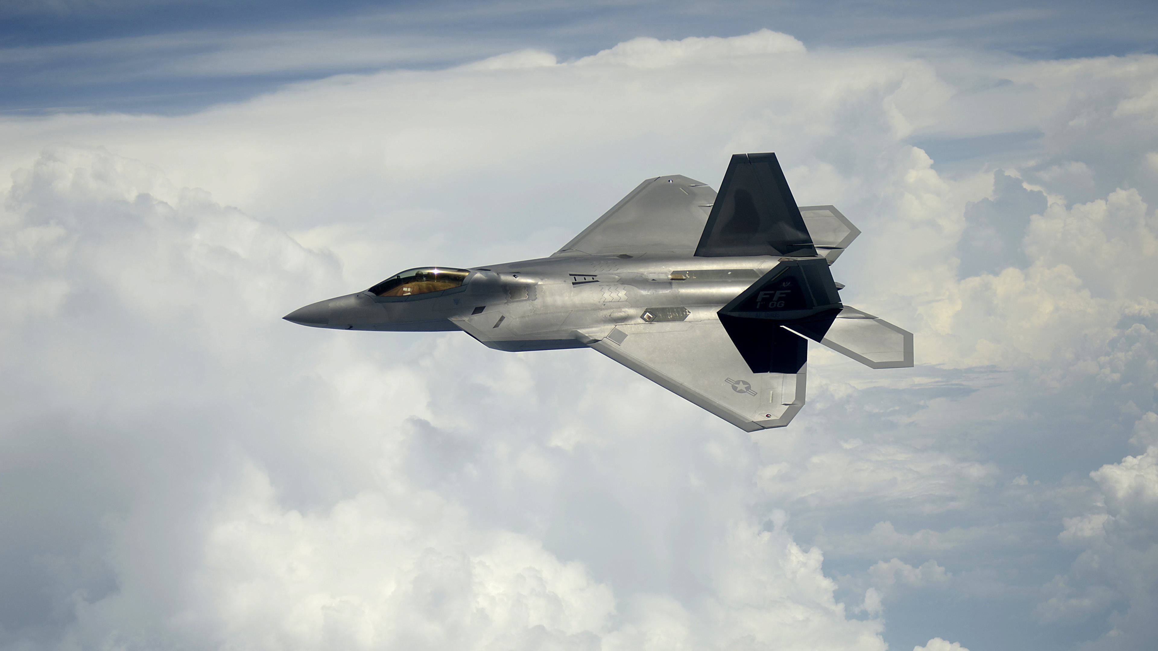4K 飛機壁紙 桌布 壁紙 — 一架流線型灰色F-22猛禽戰鬥機在明亮的藍天下翱翔於蓬鬆的白雲之上。