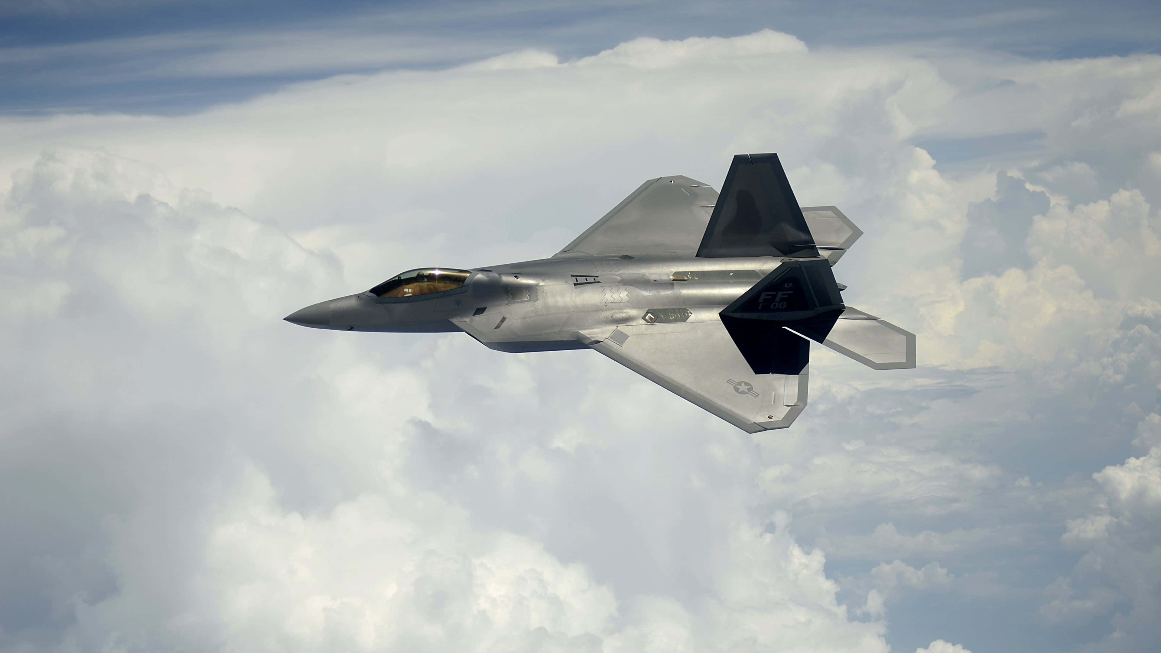 4K 飛機壁紙 桌布 壁紙 — 一架流線型灰色F-22猛禽戰鬥機在明亮的藍天下翱翔於蓬鬆的白雲之上。