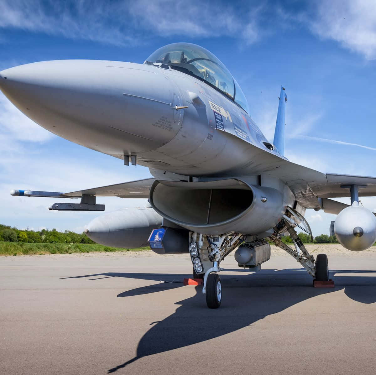 Air Force 桌布 壁紙 — 一架流線型灰色戰鬥機搭載飛彈，停在停機坪上，背景是晴朗藍天和零星白雲。