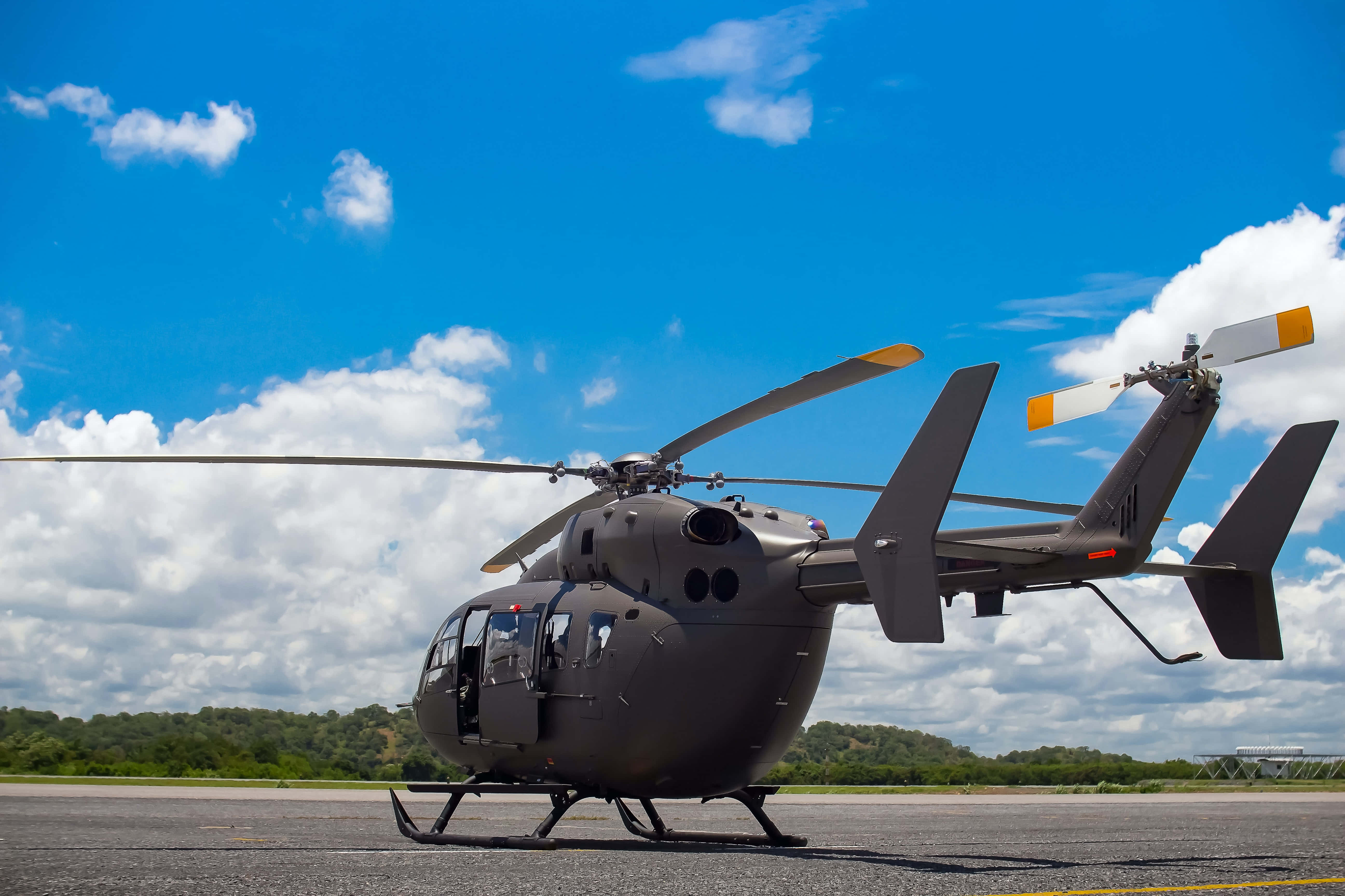 Helicopter 桌布 壁紙 — 一架流線型灰色直升機停在停機坪上，背景是晴朗的藍天，點綴著蓬鬆的白雲。