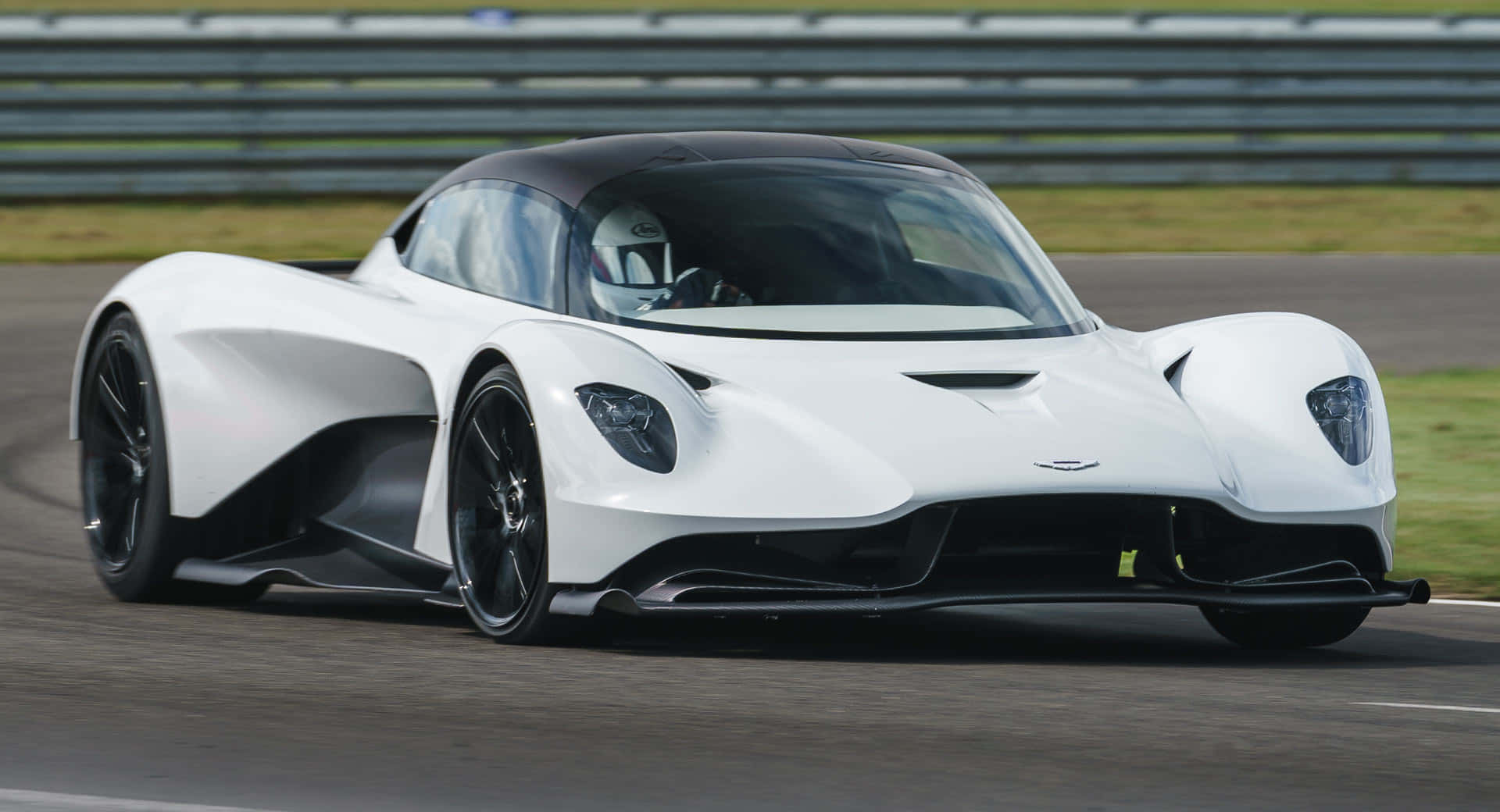 奧斯頓馬丁 桌布 壁紙 — 一架流線型白色Aston Martin Valkyrie賽車在賽道上疾馳，背景有模糊的動感和綠色草地。