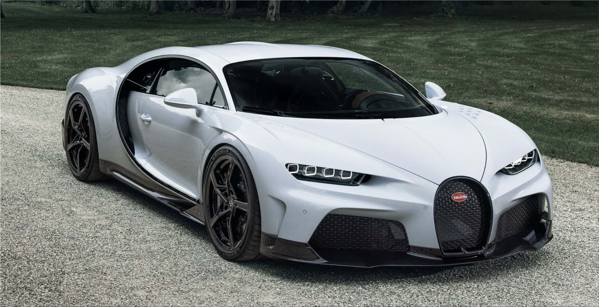 布加迪 桌布 壁紙 — 一架流線型白色Bugatti Chiron，剪刀門打開，停泊在草地旁邊的碎石路上。