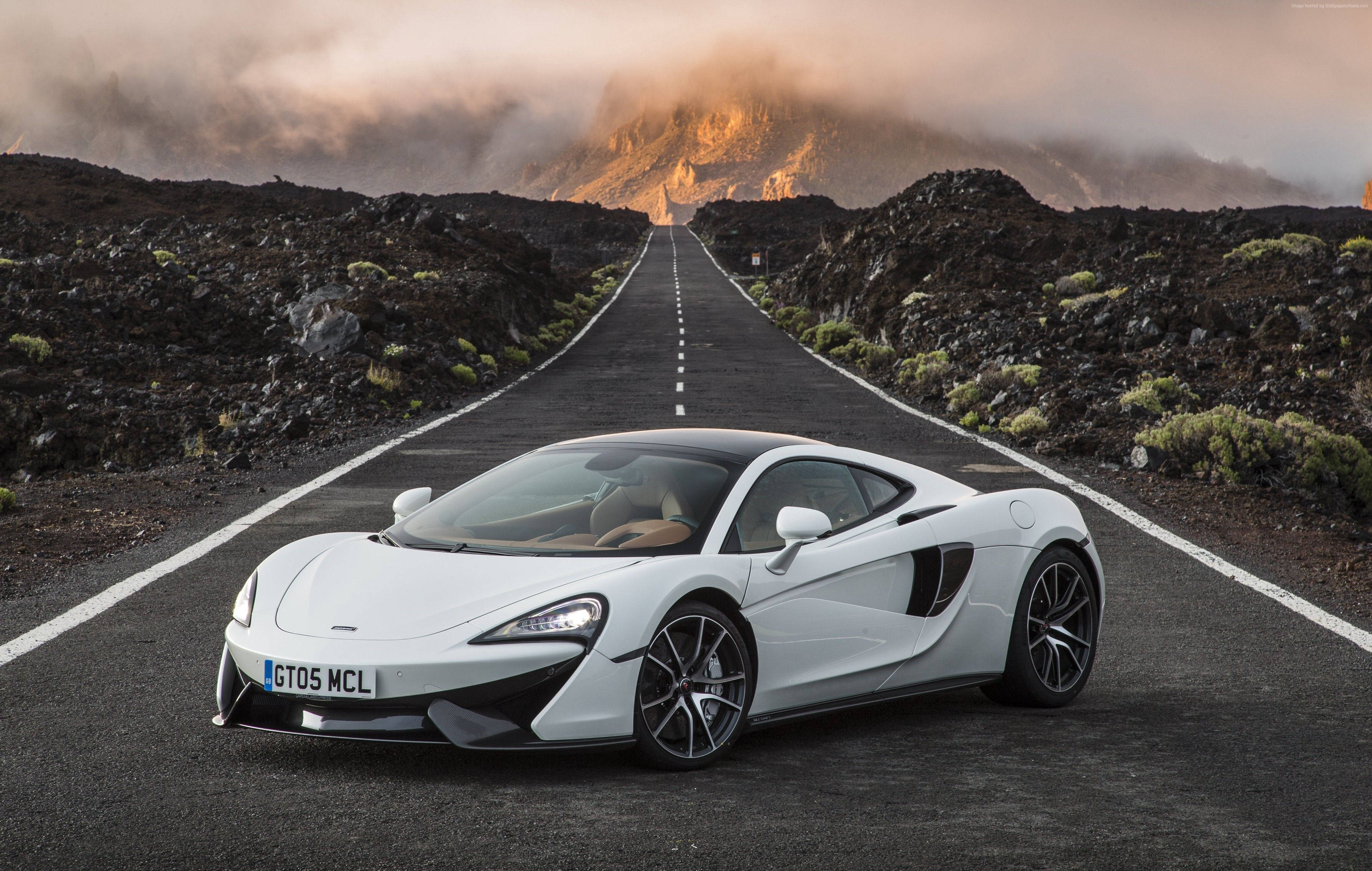 麥拉倫 桌布 壁紙 — 一架流線型白色McLaren跑車在日落時分，停在一條穿越崎嶇火山景觀的直路上。
