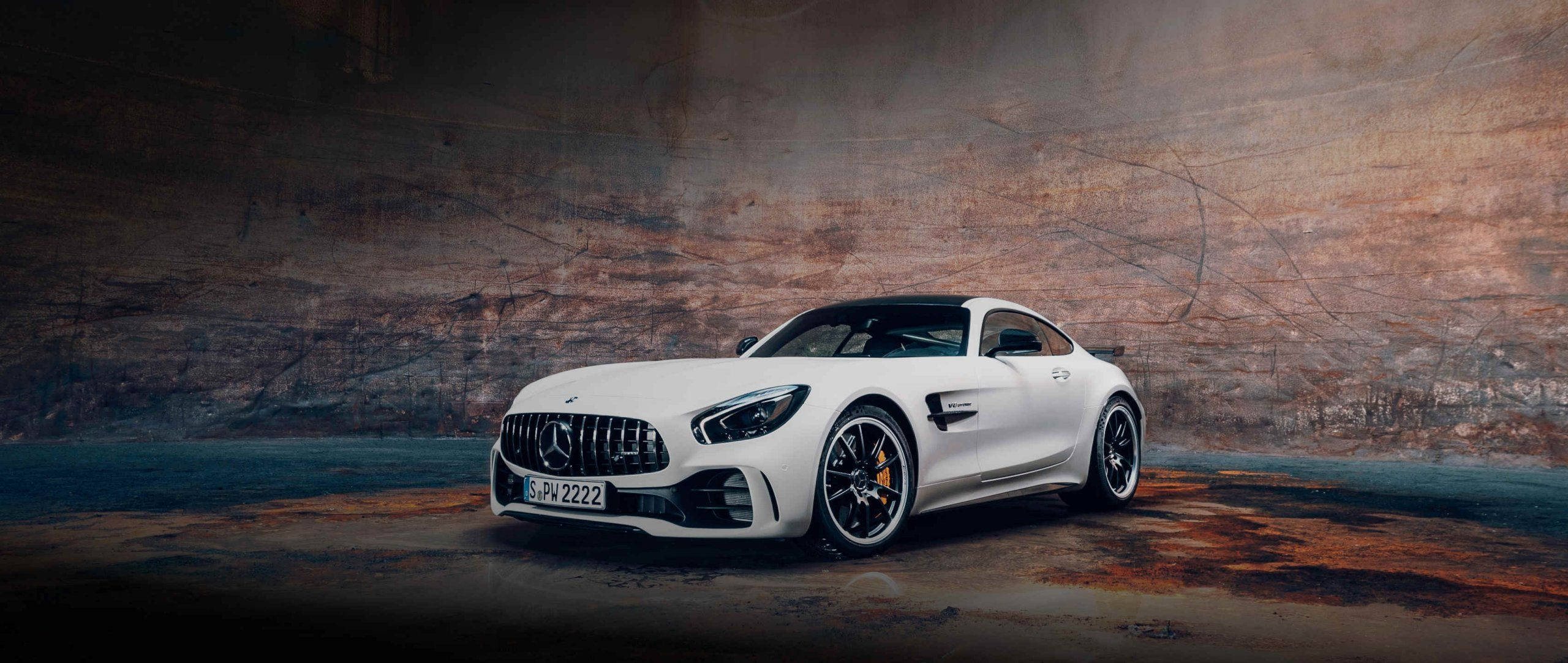 Mercedes 桌布 壁紙 — 一架流線型白色Mercedes-AMG GT停放在燈光昏暗、帶有紋理混凝土牆的工業空間。