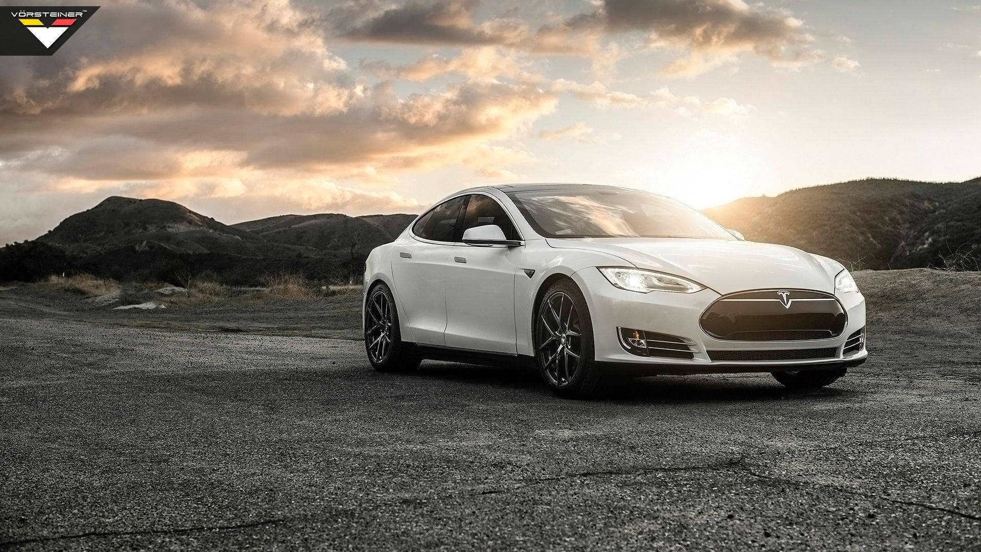 特斯拉 桌布 壁紙 — 一架流線型白色Tesla Model S停放在裂開的柏油路上，背後有起伏的山丘和戲劇性的金色日落雲彩。