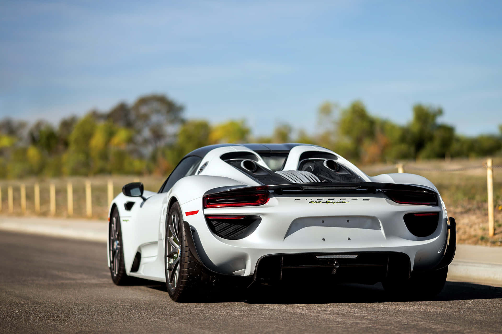 白色保時捷918 Spyder跑車在陽光普照的道路上，背景有樹木。 — 保時捷 GIF 壁紙