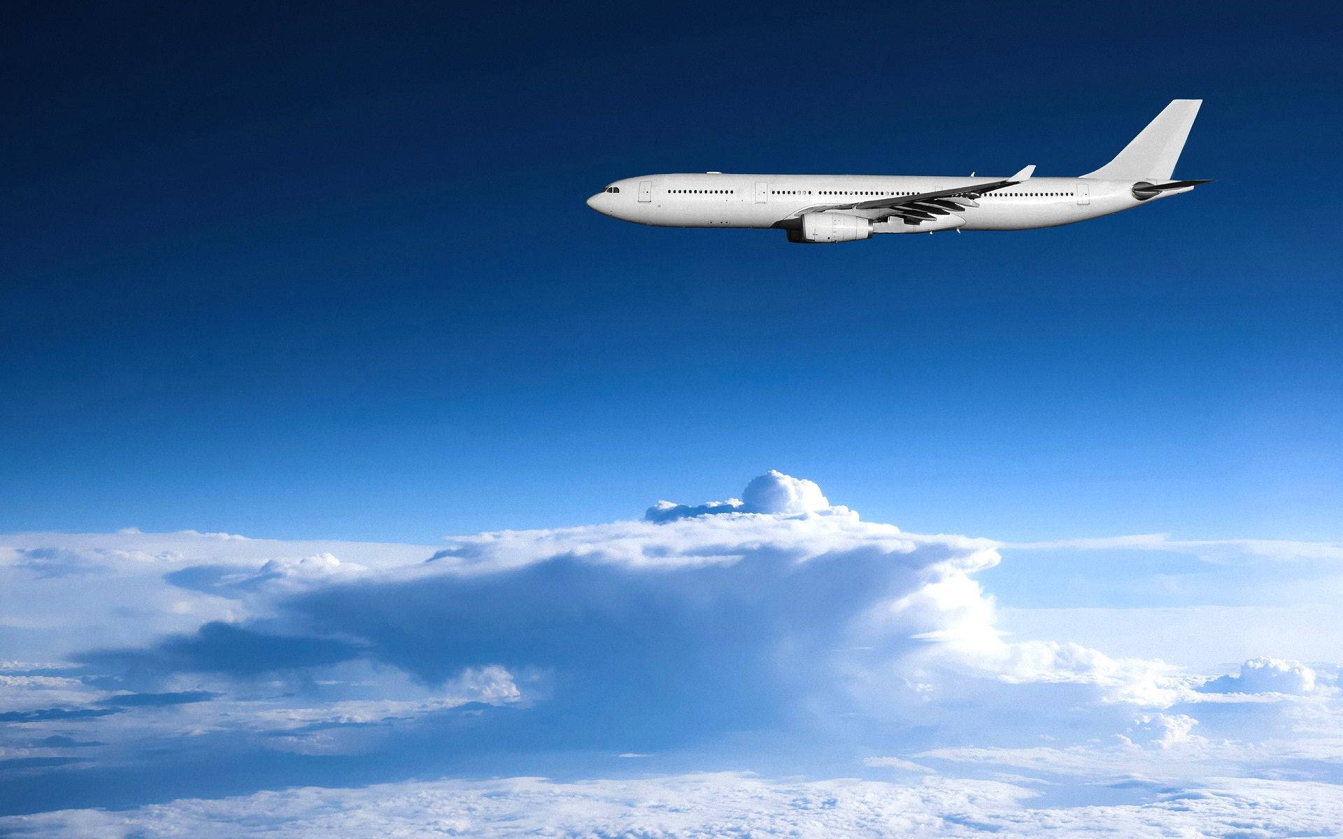 飛機 桌布 壁紙 — 一架流線型白色客機在廣闊清澈的藍天下，翱翔於蓬鬆的白雲之上。