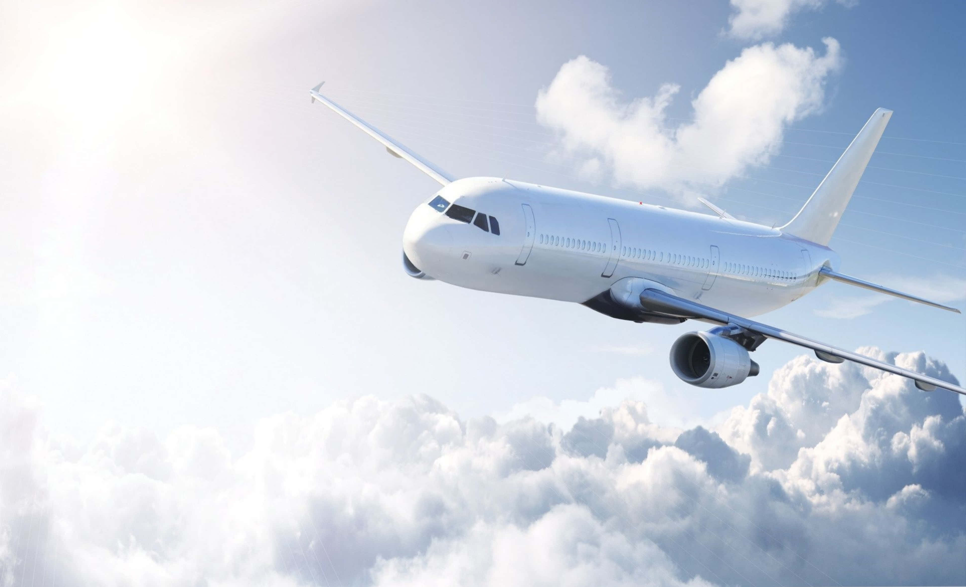 Plane 桌布 壁紙 — 一架流線型白色客機在明亮的藍天下優雅地翱翔於蓬鬆的白雲之上。