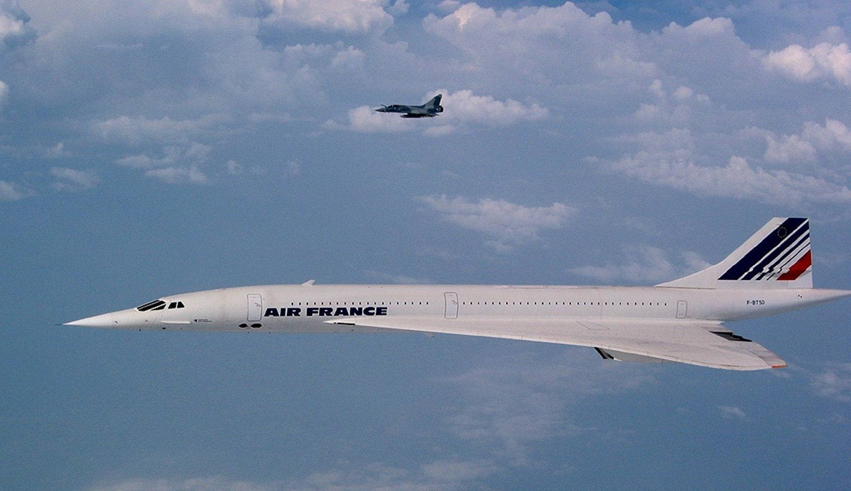 Plane 桌布 壁紙 — 一架流線型白色法國航空和諧式超音速噴射機在點綴著蓬鬆白雲的明亮藍天中翱翔，附近有一架較小的戰鬥機飛行。