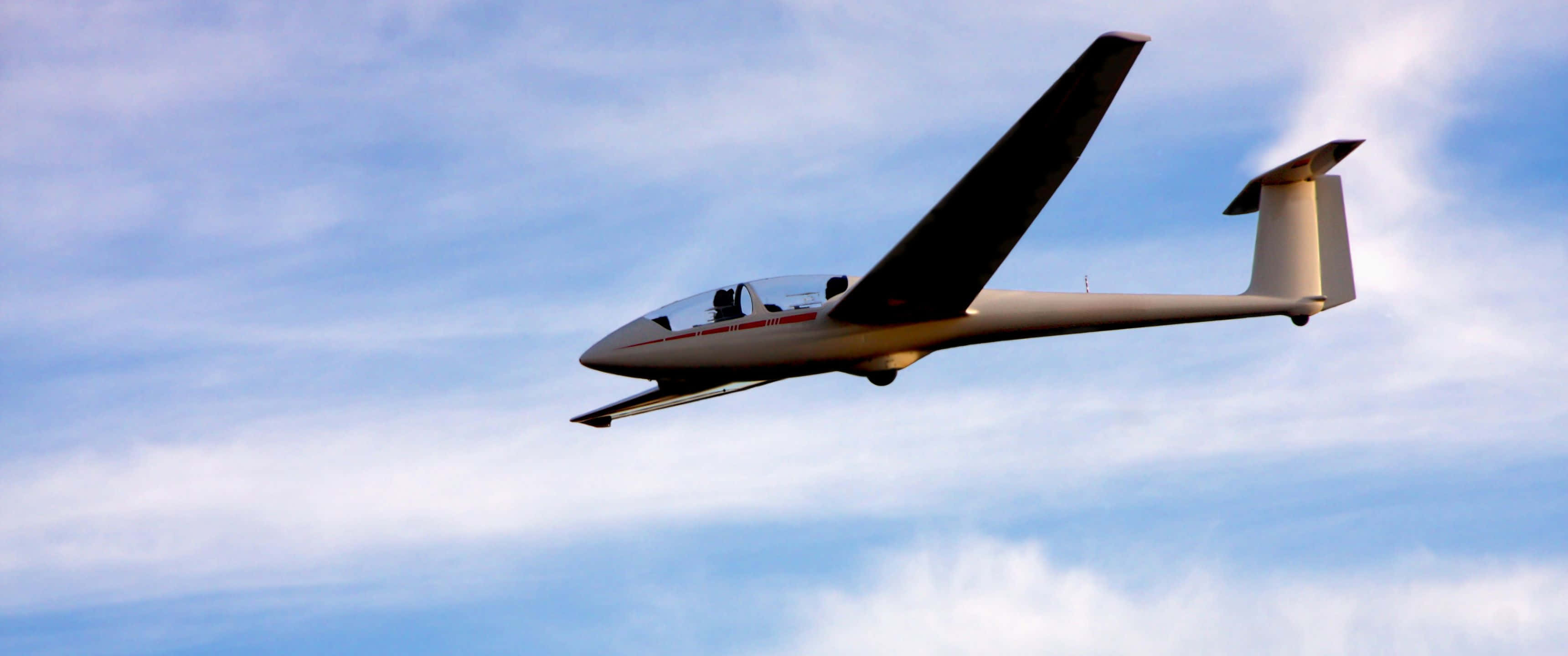 3440x1440p Small Planes 桌布 壁紙 — 一架流線型白色滑翔機在點綴著縷縷白雲的明亮藍天中優雅翱翔。