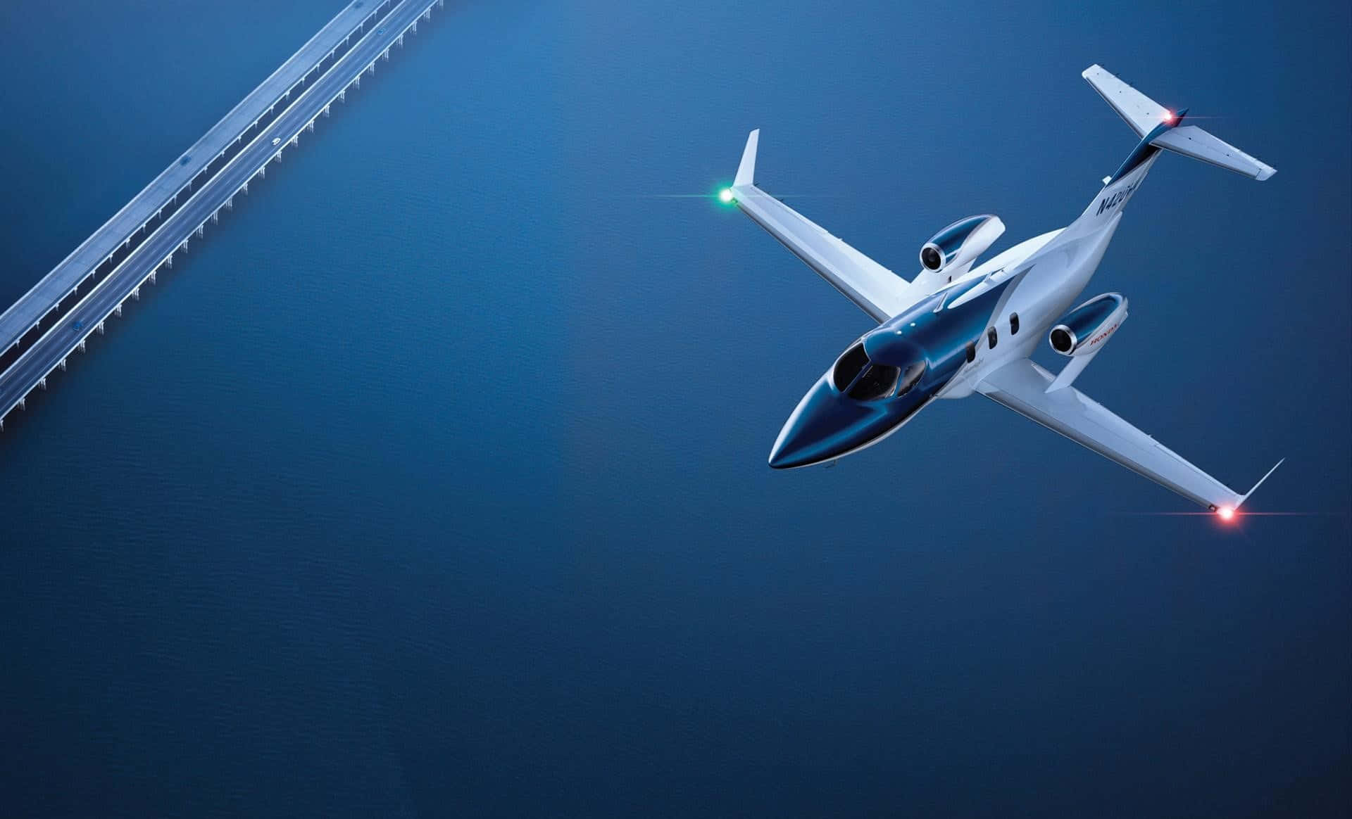Flight 桌布 壁紙 — 一架流線型白色私人飛機低飛過深藍色水面，遠處有一座長橋延伸至天際。
