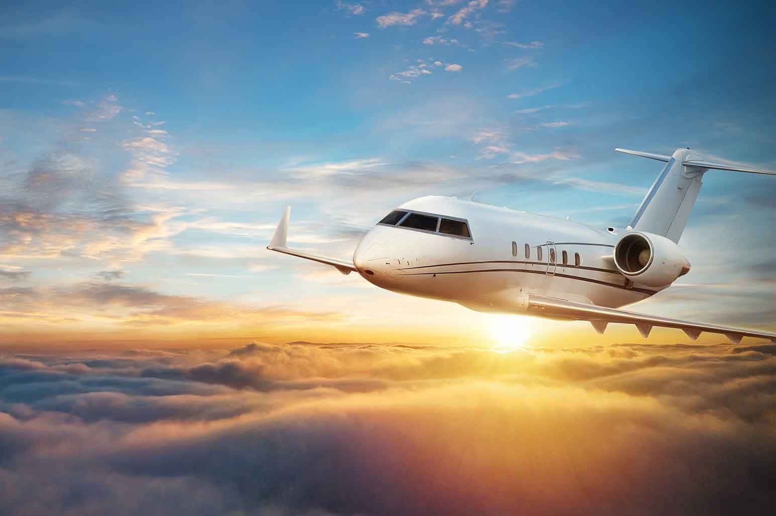 飛機 桌布 壁紙 — 一架流線型白色私人飛機在金色雲層上方翱翔，太陽從其後升起，將溫暖的光芒灑向天空。
