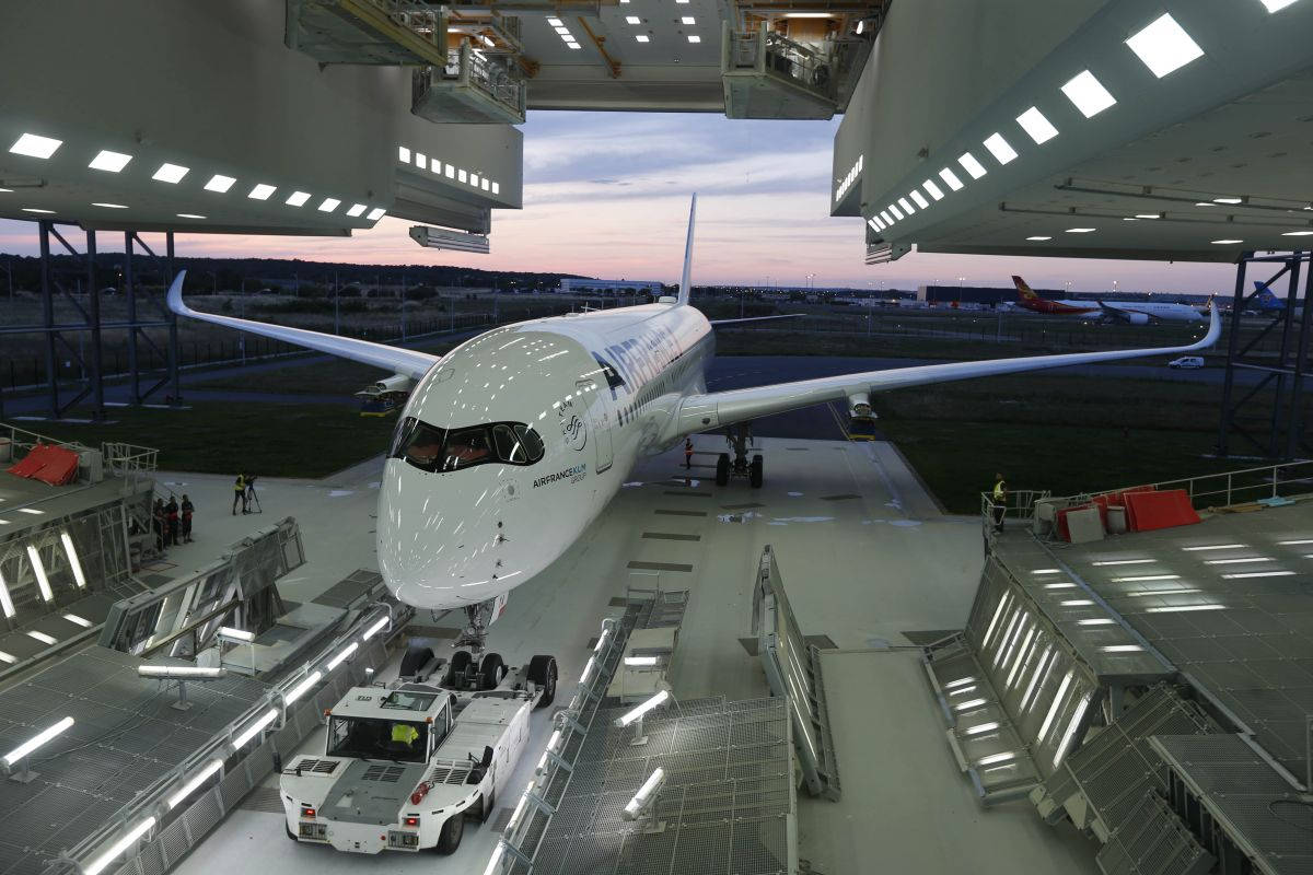  壁紙 — 一架流線型白色空中巴士A350停放在寬敞的機庫內，附近有工人和地面車輛，正值黃昏時分。