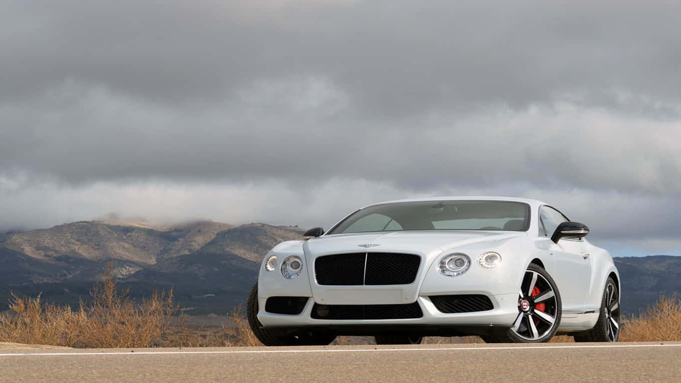 1366x768 Bentley 桌布 壁紙 — 一架流線型白色賓利 Continental GT 雙門跑車停靠在路邊，背景是崎嶇的山脈和陰天。