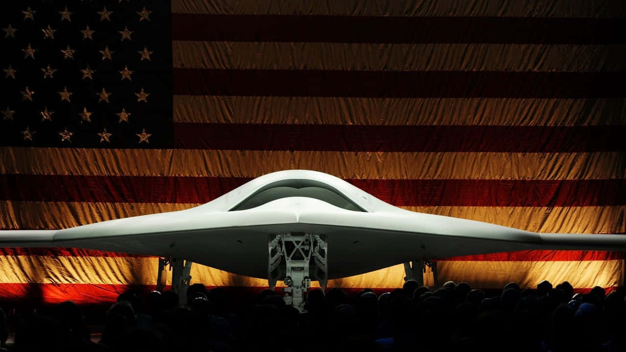 飛機 桌布 壁紙 — 一架流線型白色隱形戰機在大型美國國旗前戲劇性地展示，人群以剪影觀看。