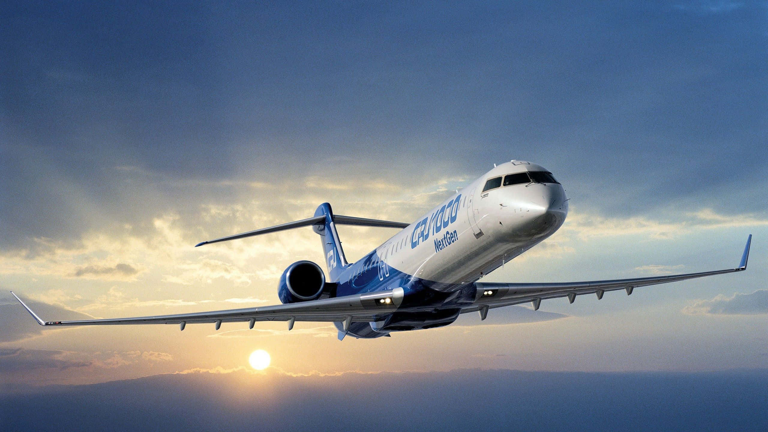 桌布 壁紙 — 一架流線型的CRJ NextGen區域噴射機在戲劇性的日落天空中翱翔，下方有金色的雲朵和發光的太陽。