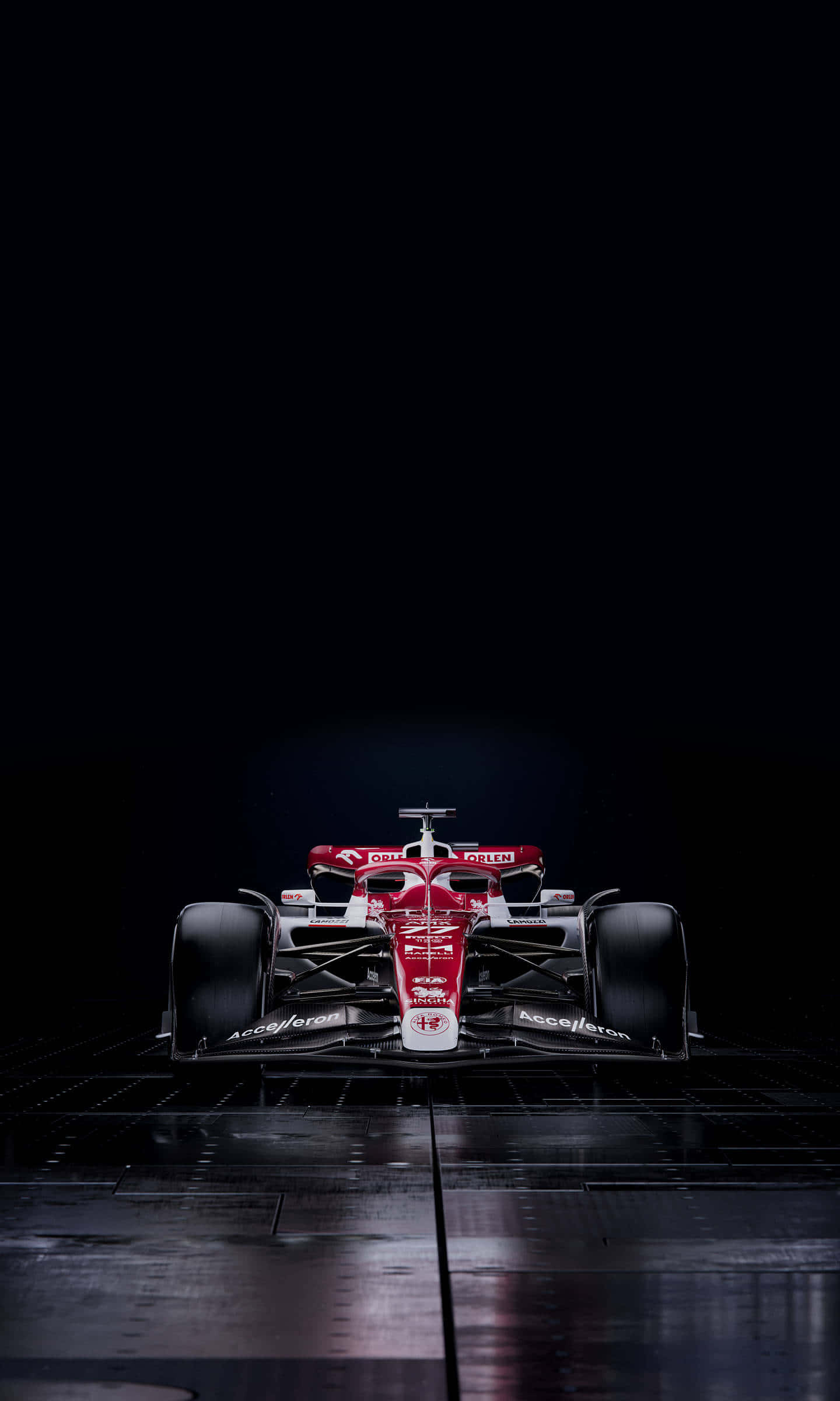 Formula 1 iPhone 桌布 壁紙 — 一架流線型的紅黑一級方程式賽車在黑色背景的深色網格地板上從上方戲劇性地照亮。