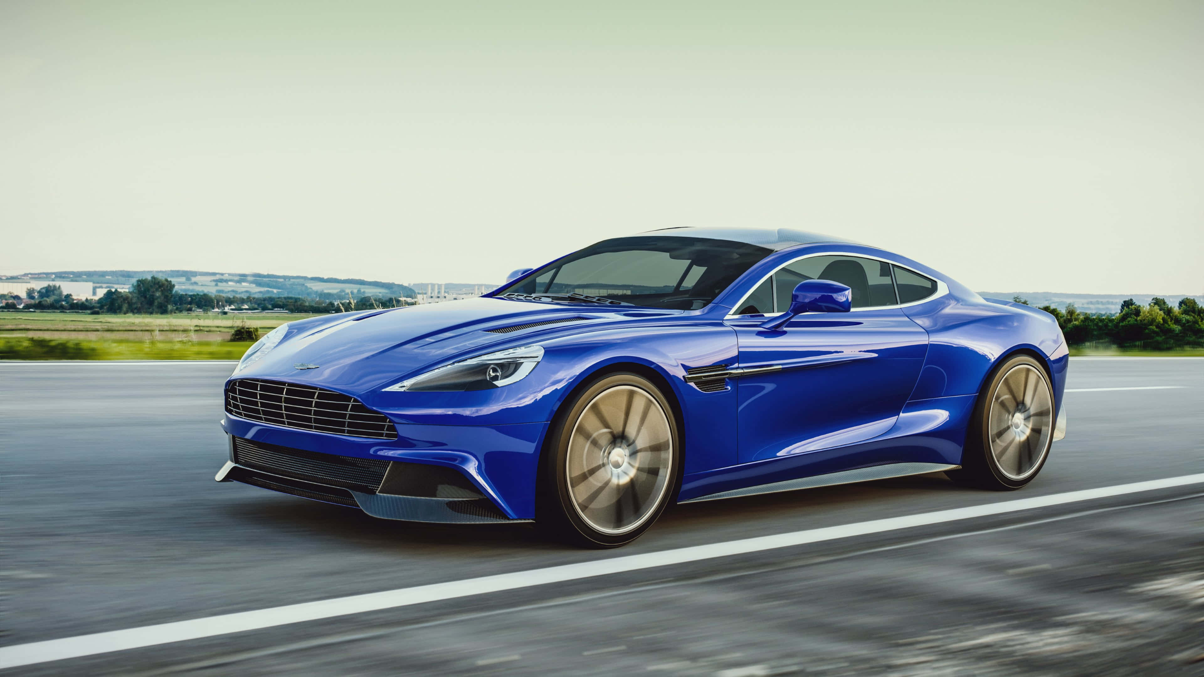 奧斯頓馬丁 桌布 壁紙 — 一架流線型的藍色Aston Martin跑車在柔和日光的天空下沿鄉村高速公路飛馳。