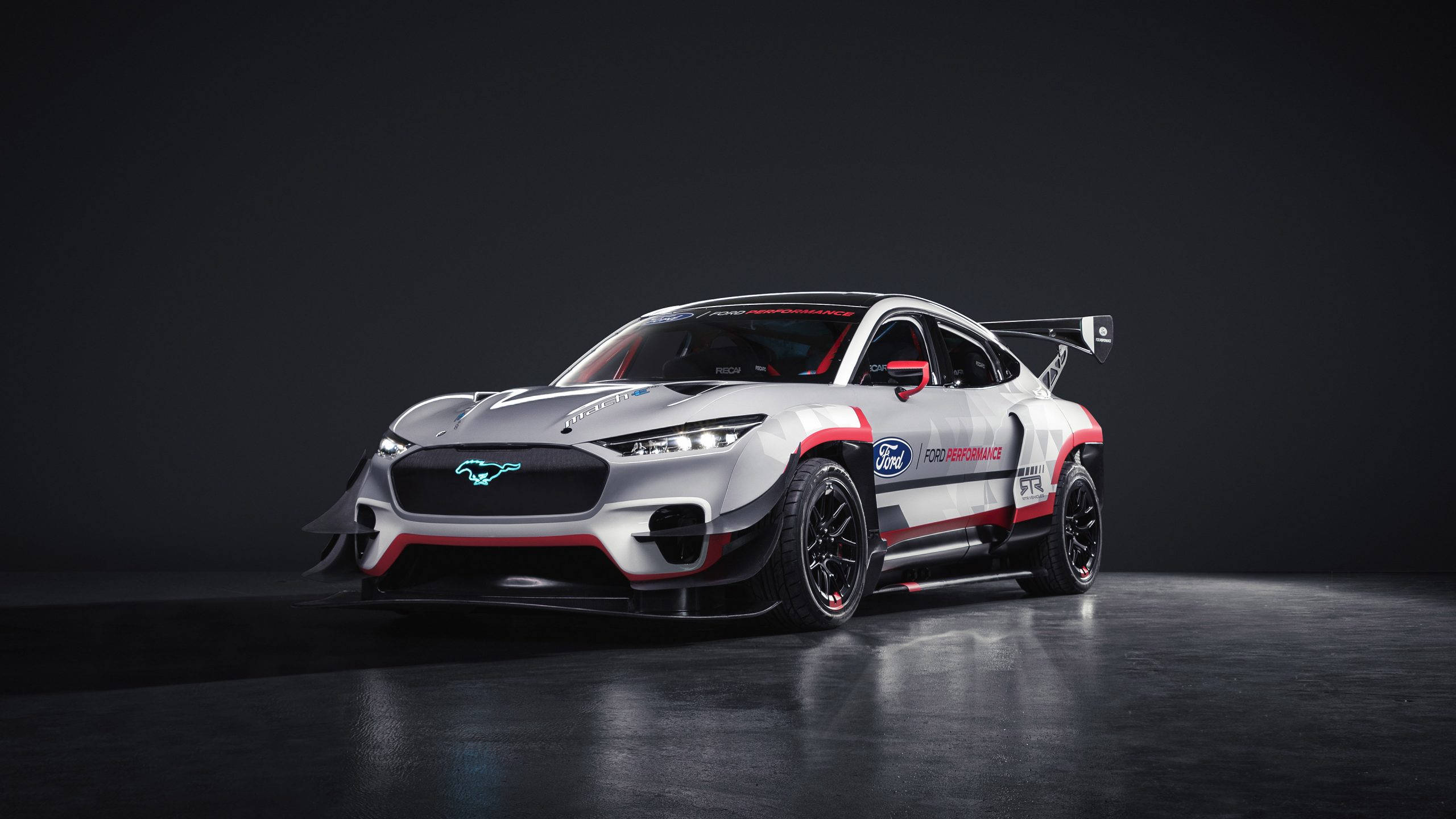 Cool Mustang 桌布 壁紙 — 一架流線型的銀色福特野馬GT4賽車，帶有紅色點綴和發光的車頭燈，在黑暗的攝影棚背景下戲劇性地照亮。