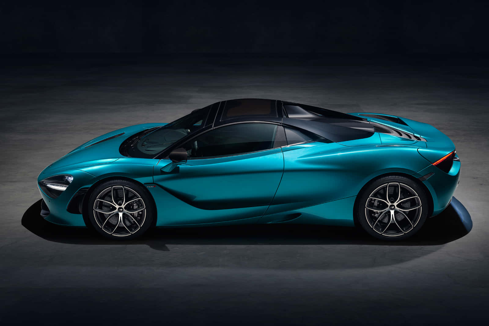 Blue Car 桌布 壁紙 — 一架流線型的青綠色McLaren 720S超級跑車在昏暗的攝影棚中滑行，戲劇性的聚光燈凸顯其空氣動力學曲線。