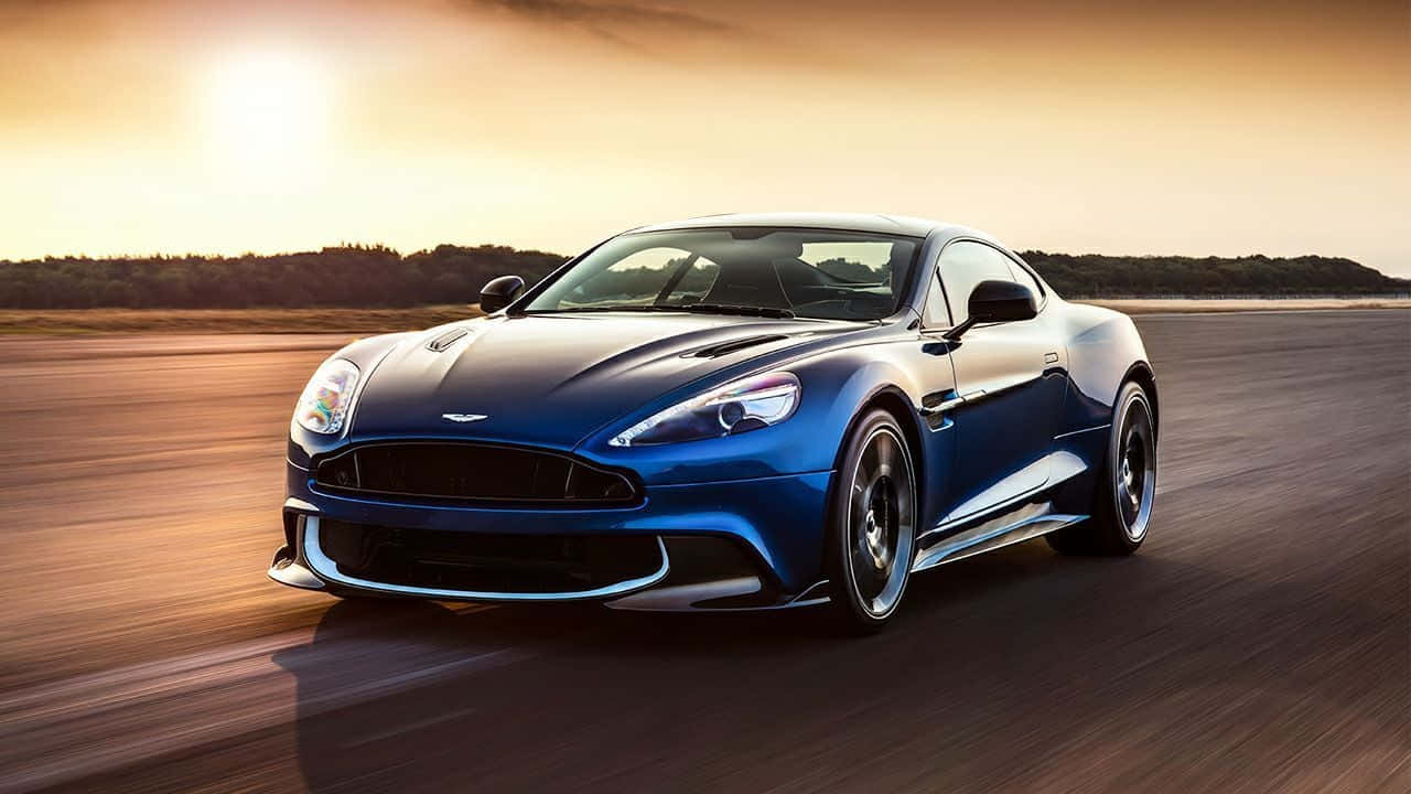 Aston Martin Vanquish 桌布 壁紙 — 一架流線型藍色Aston Martin跑車在日落時分沿著跑道疾馳，帶有動態模糊和金色光線。