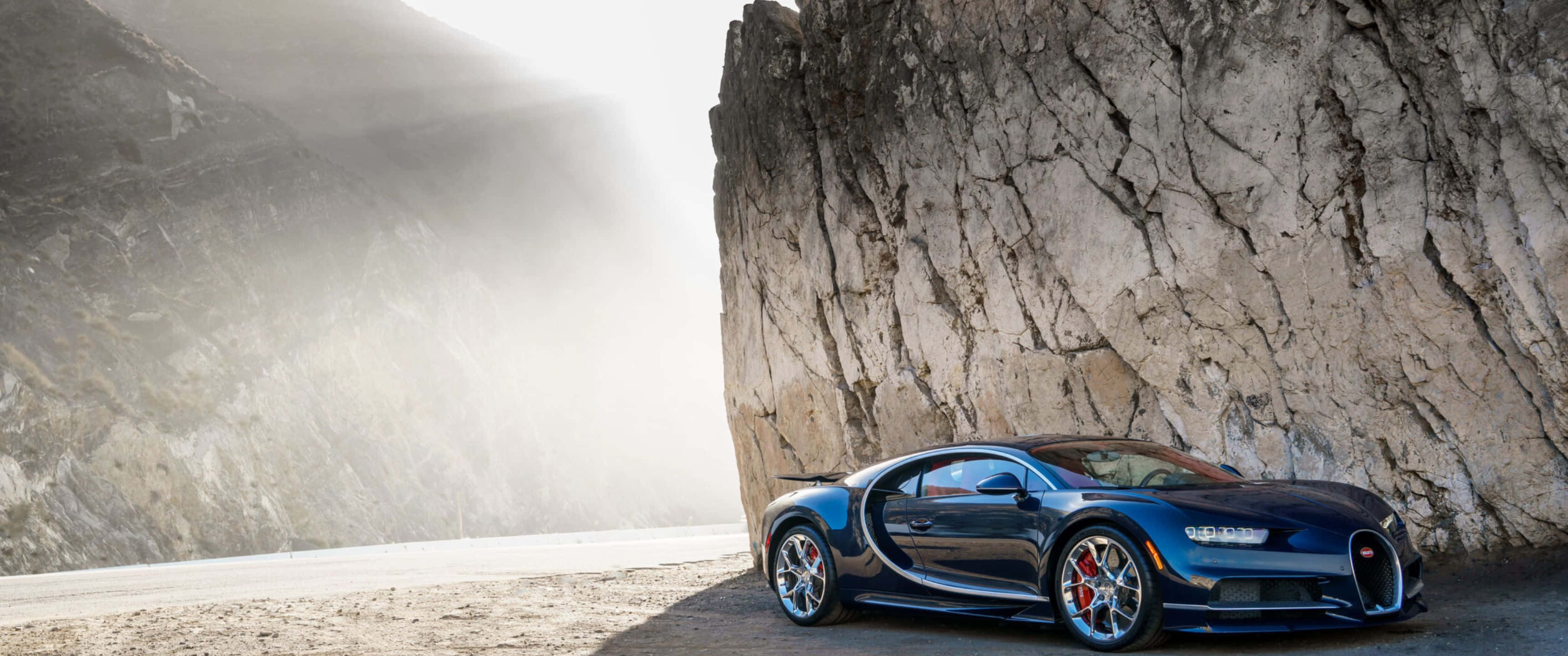 3440x1440p Bugatti 桌布 壁紙 — 一架流線型藍色Bugatti超跑停泊在霧氣瀰漫的山路上，旁邊是高聳的岩石峭壁。