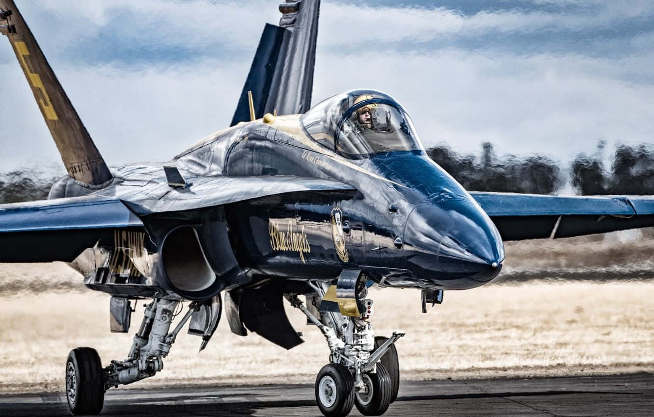 US Navy 桌布 壁紙 — 一架流線型藍色戰鬥機帶有金色點綴，在陰天下的跑道上滑行，駕駛艙內可見飛行員。