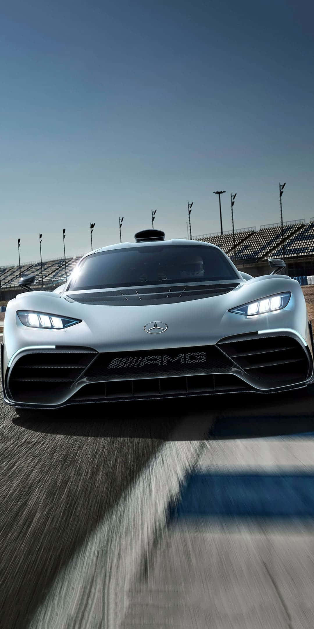 cars 桌布 壁紙 — 一架流線型銀色 Mercedes-AMG 賽車在晴朗藍天下的賽道上疾馳，動態模糊強調了速度。