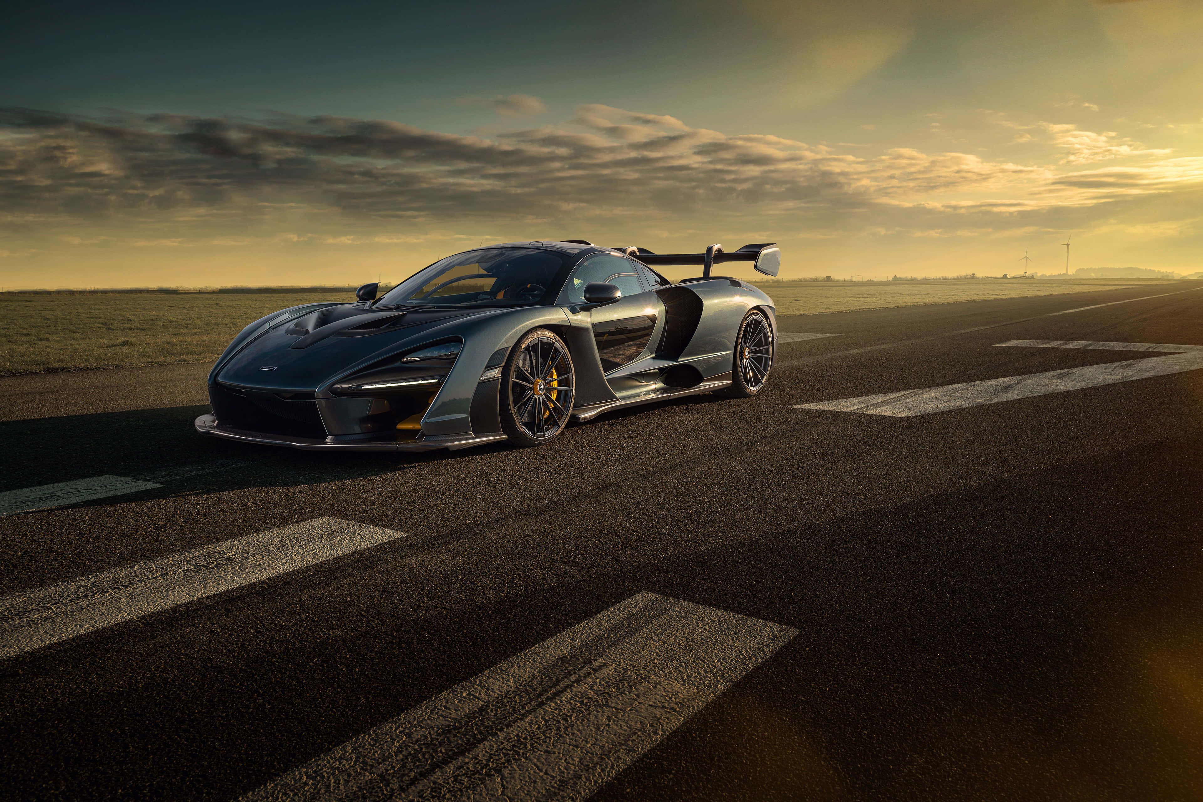 Cool Mclaren 桌布 壁紙 — 一架流線型銀色McLaren Senna跑車打開車門，停在空無一人的跑道上，正值黃金時刻，天空佈滿戲劇性的雲彩。