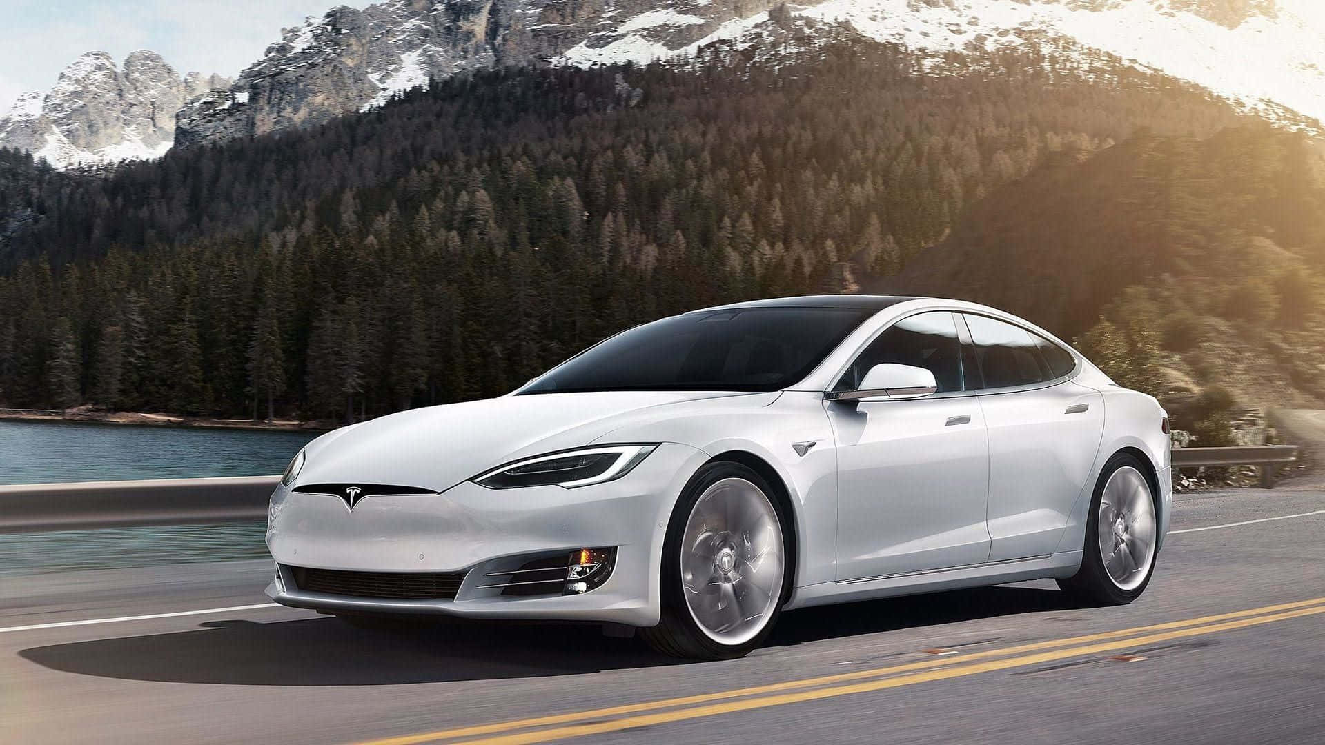 Hybrid Car 桌布 壁紙 — 一架流線型銀色Tesla Model S沿著湖邊的山路行駛，背景是白雪覆蓋的山峰和茂密的松樹林。