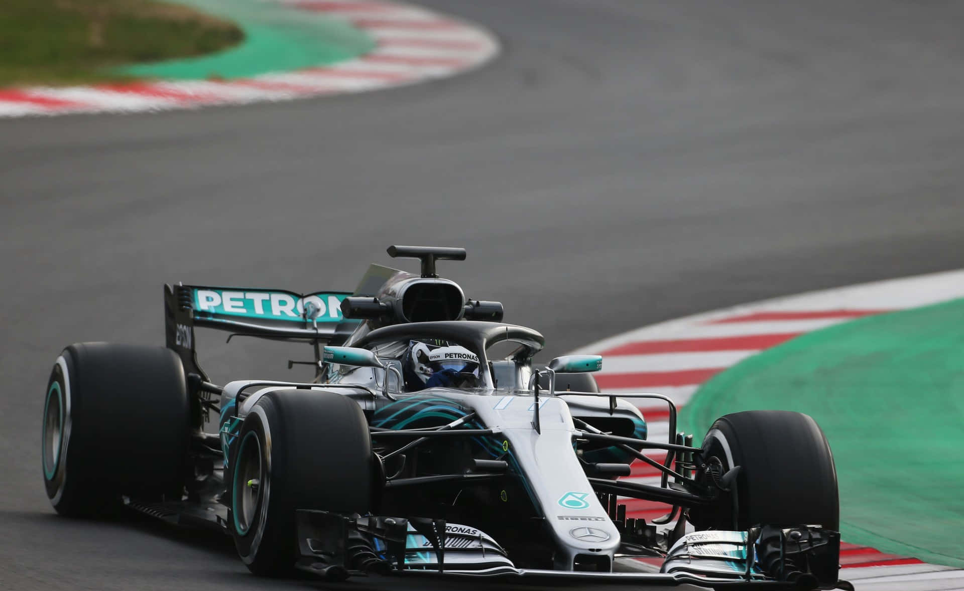 F1 2018 桌布 壁紙 — 一架流線型銀色和藍綠色的梅賽德斯一級方程式賽車在賽道上高速過彎，賽道邊緣有紅、白、綠三色路肩。