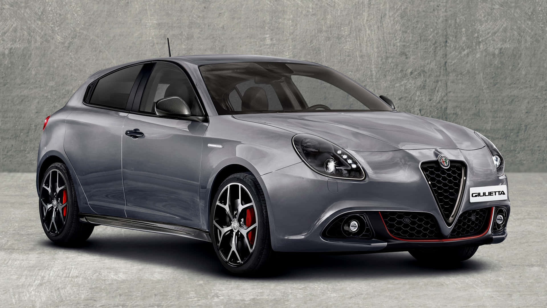 Alfa Romeo Giulietta 桌布 壁紙 — 一架流線型銀色愛快羅密歐Giulietta跑車，配備紅色制動卡鉗和黑色合金輪圈，停靠在紋理灰色混凝土牆前。